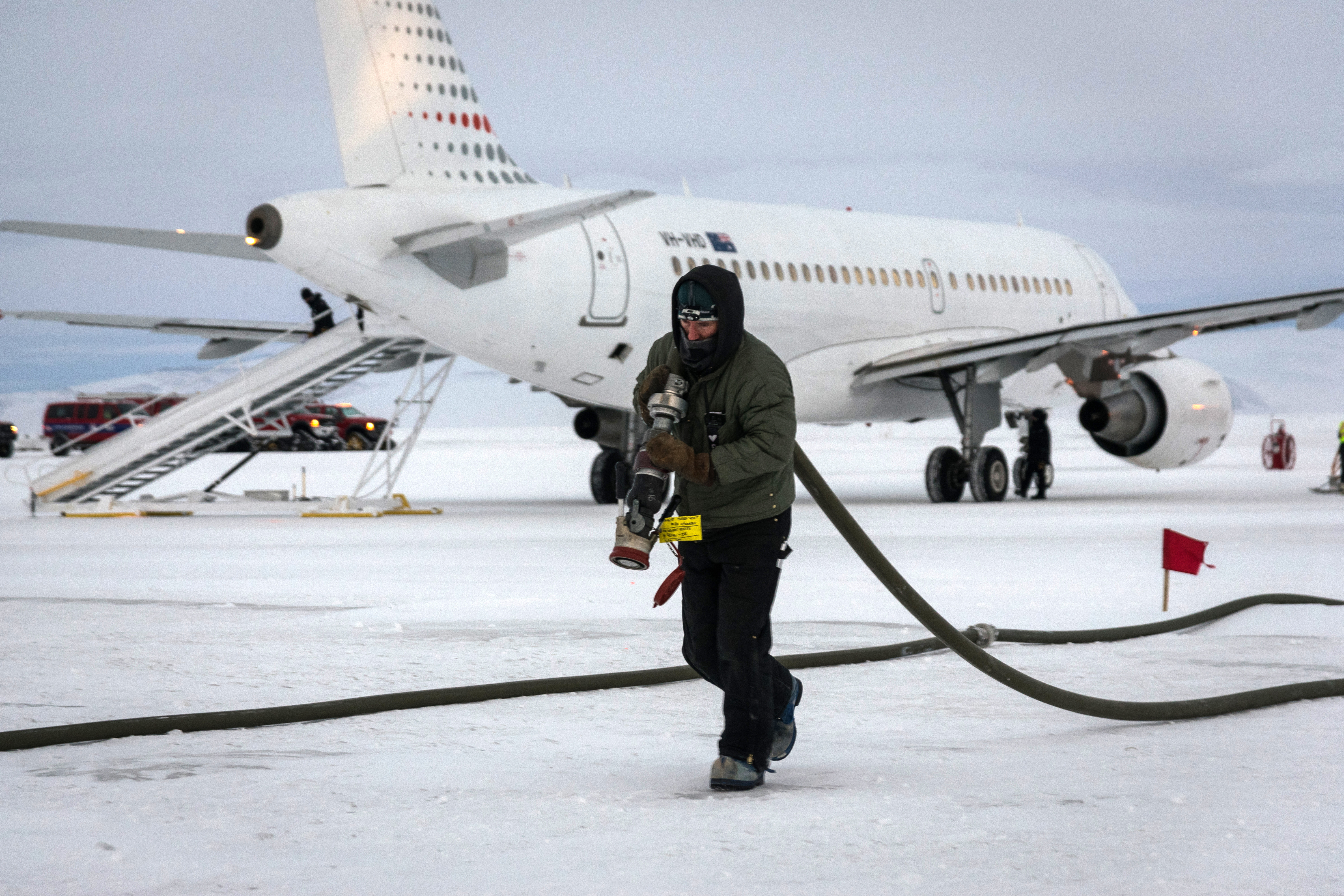 A man with a fuel hose walks away from a parked jet.