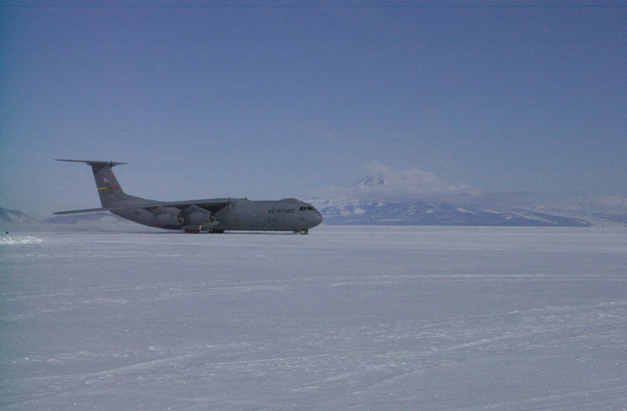 A plan is on the snow with a mountain in the background.