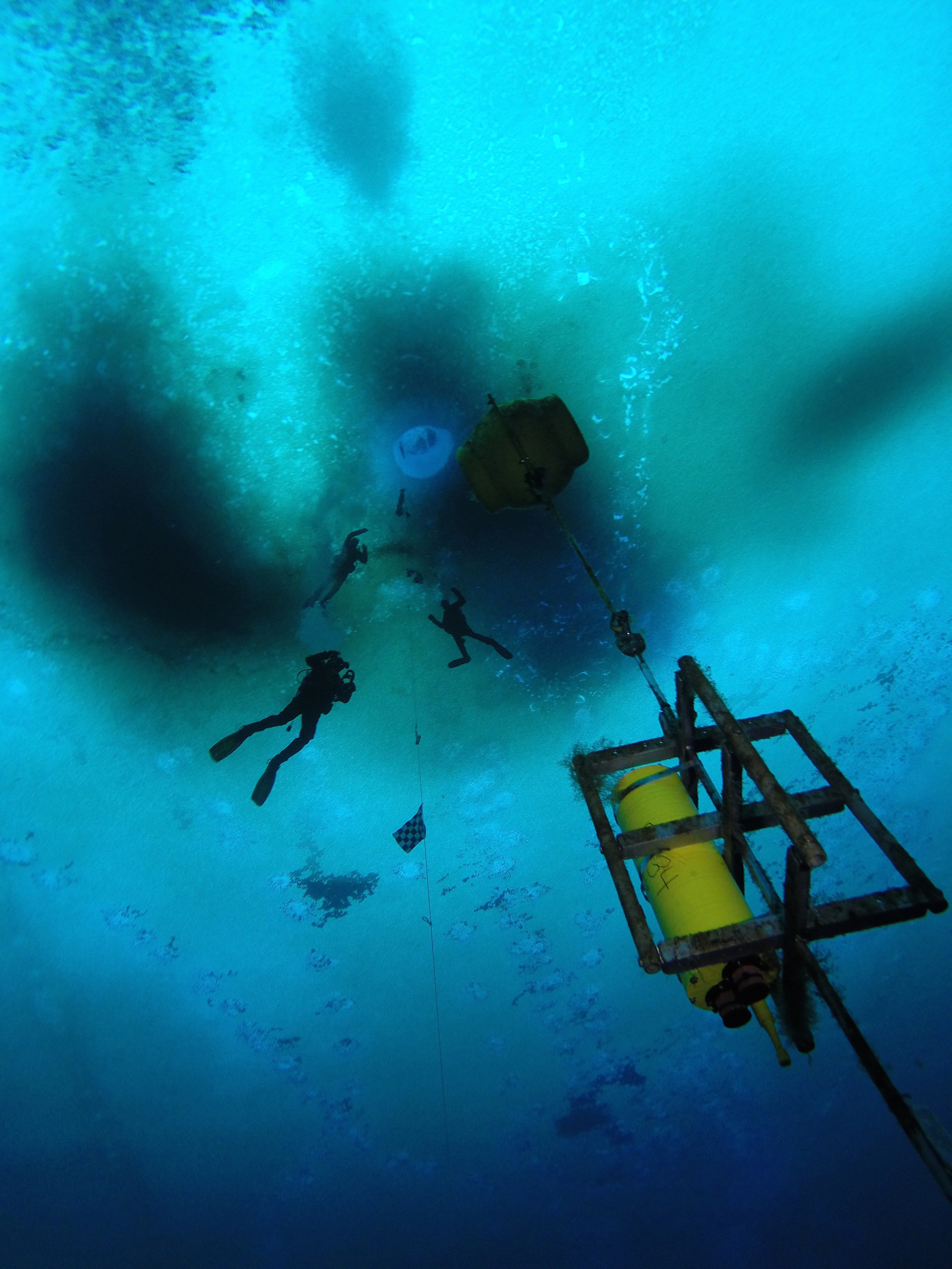 Three divers work on an instrument under frozen sea ice.