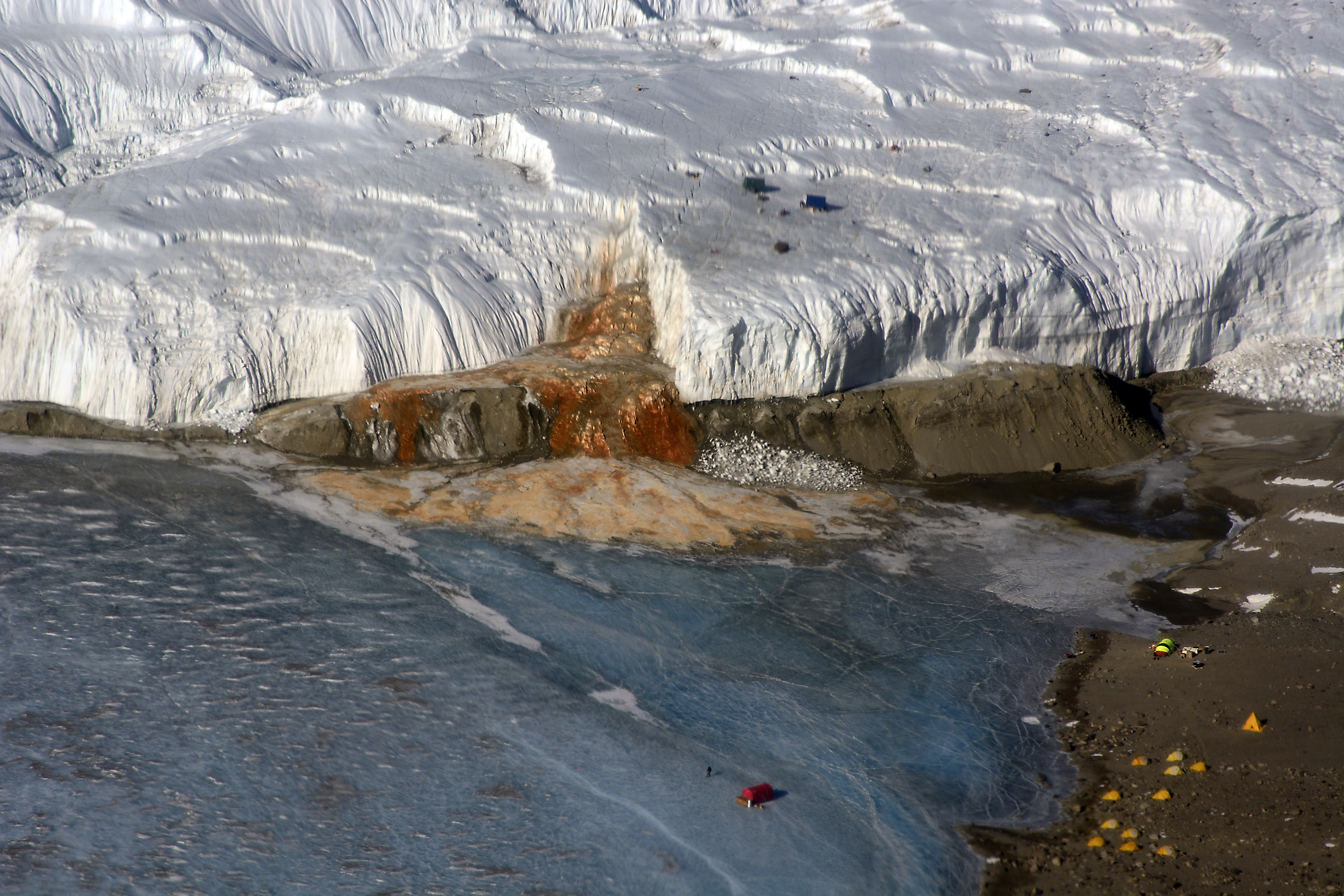 Aerial view of a glacier with a red waterfall-like feature.