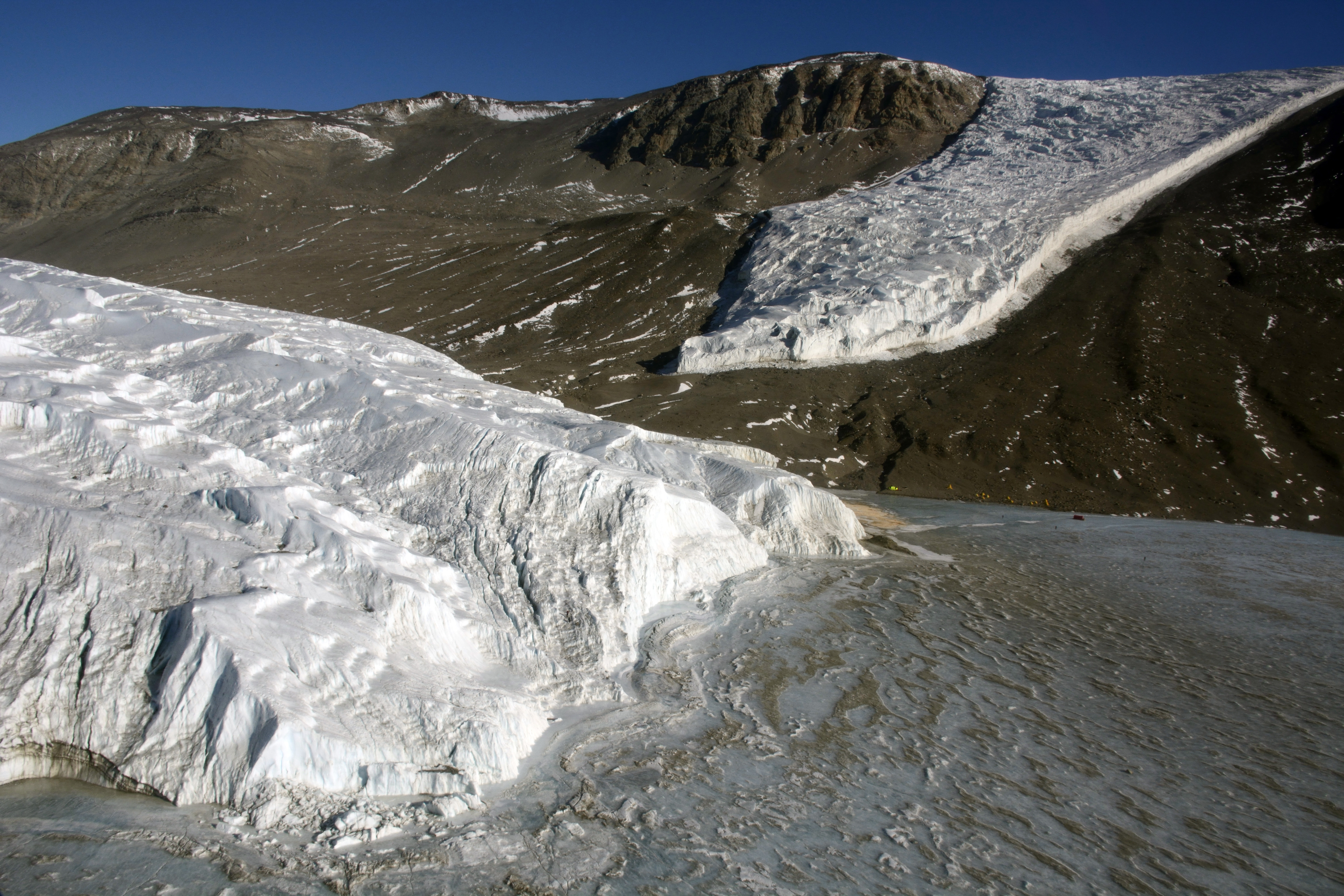 Aerial view of two glaciers and an ice-covered lake in a valley.