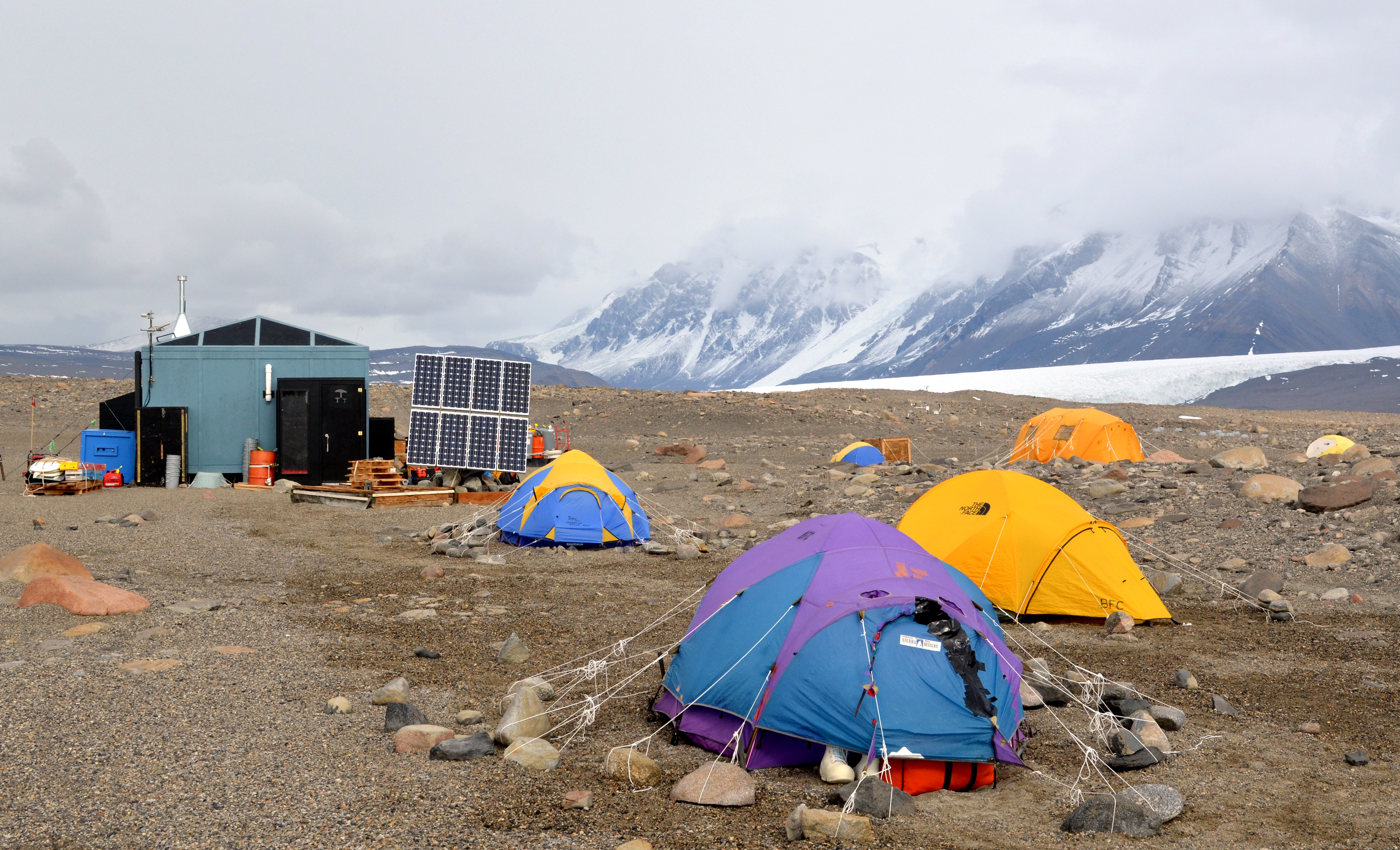 Tents and small building in rocky, cold landscape.