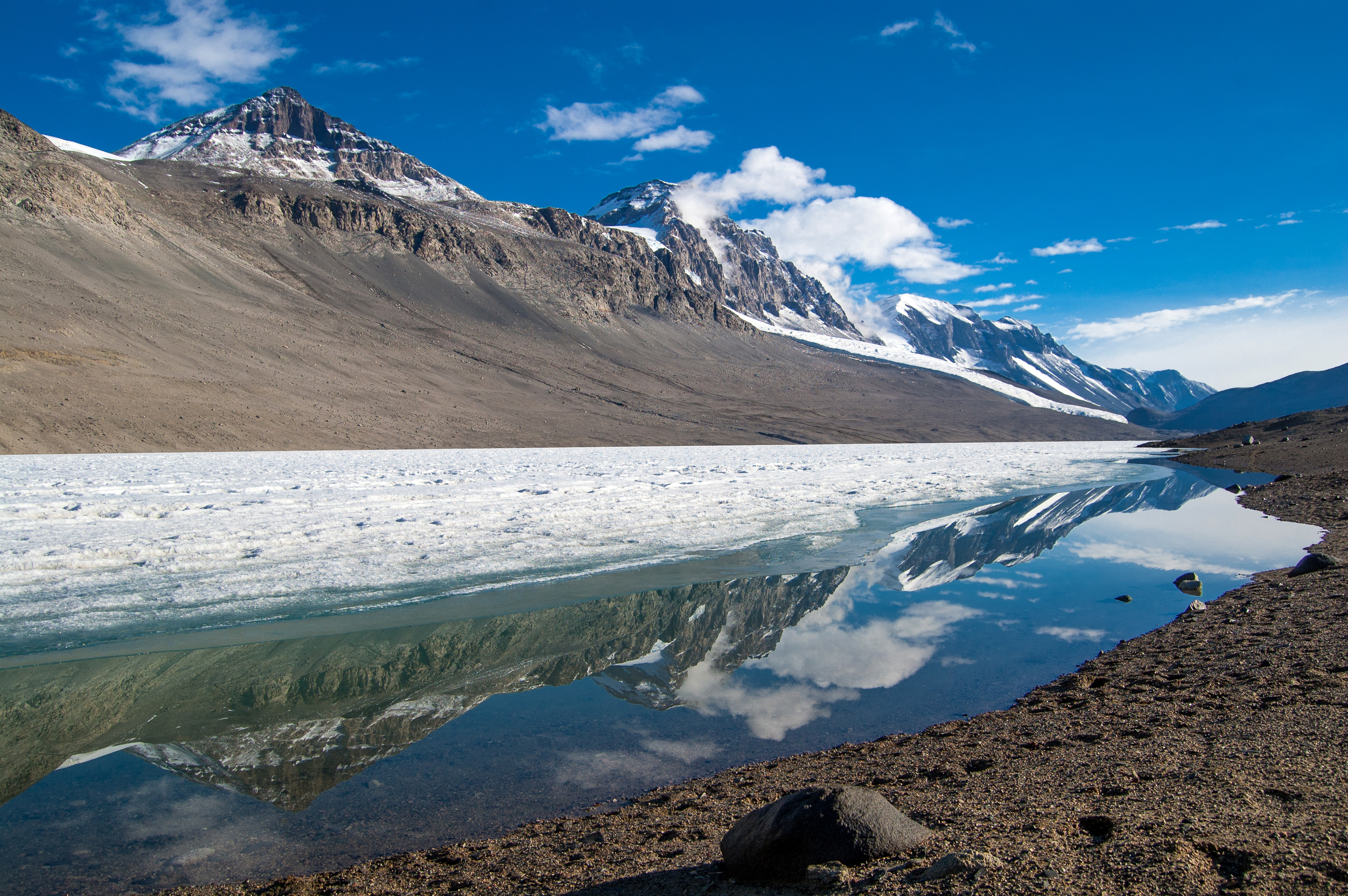 Mountains are reflected in a pool of water on valley floor.