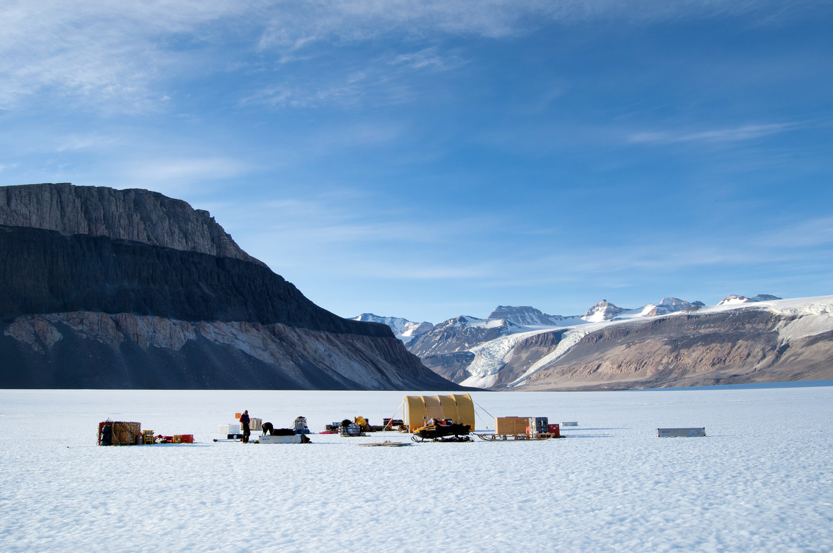 Materials sit on a plain of ice surrounded by mountains.