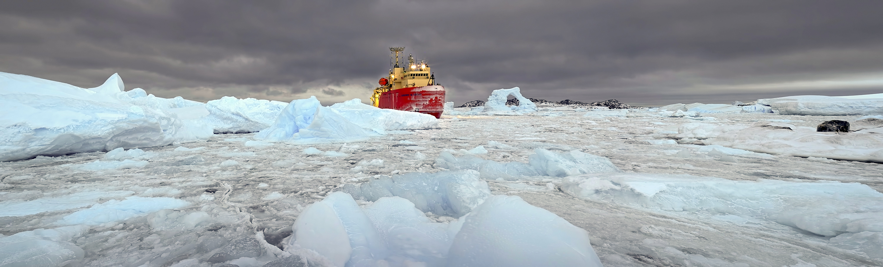 A large ship sails through ice-choked waters.
