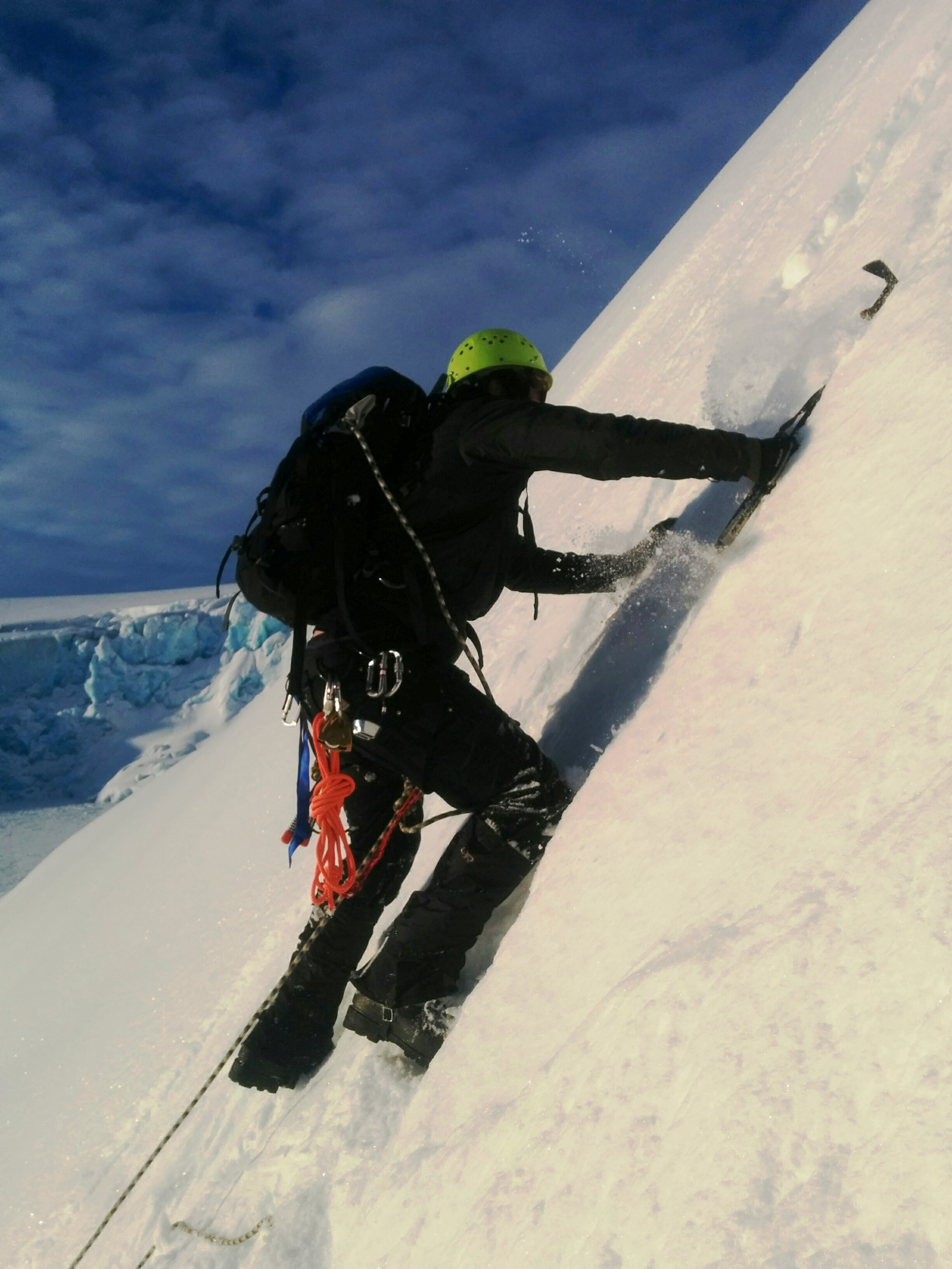 A man ascends a glacier face using an ice axe.