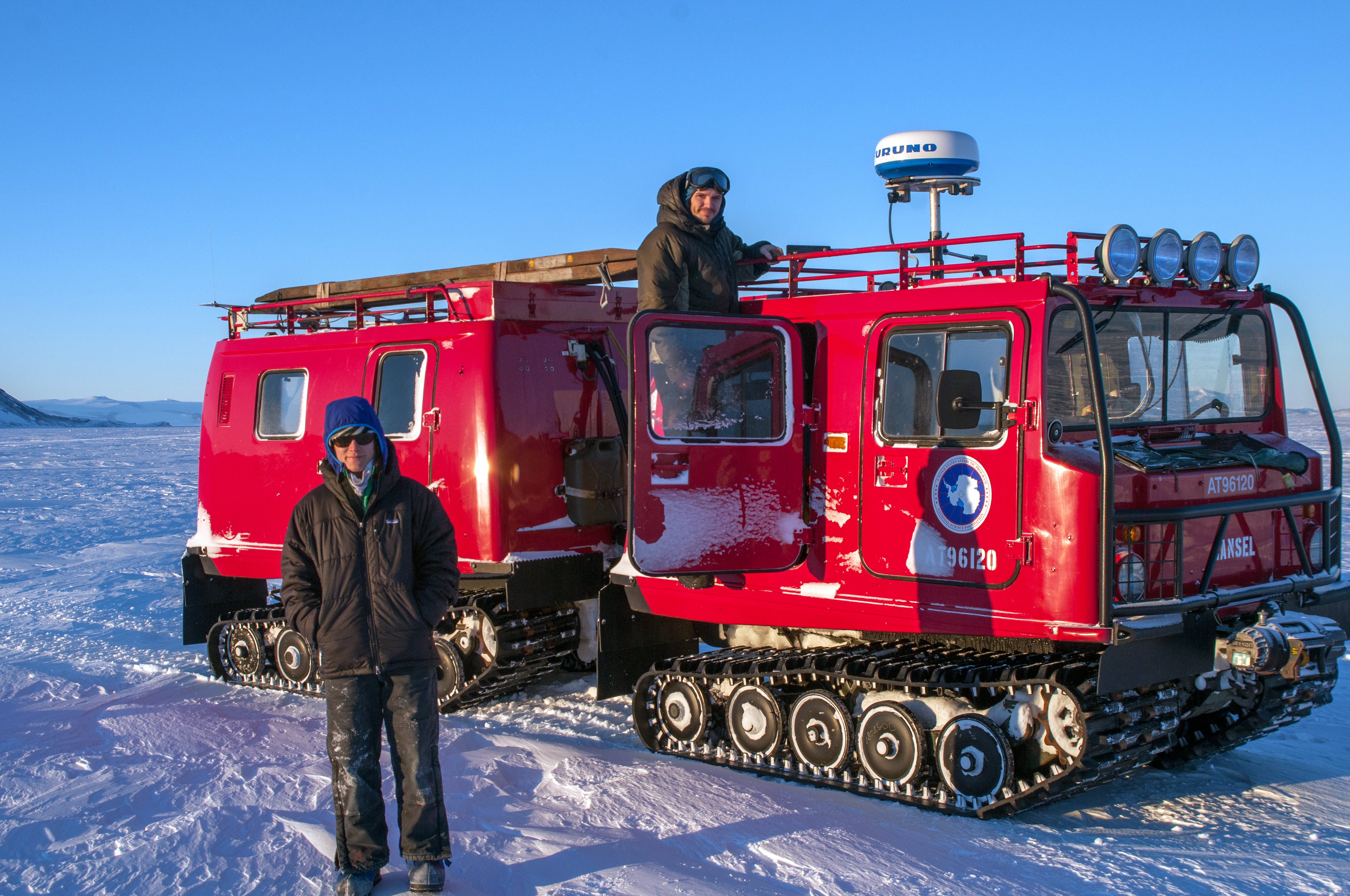 People stand near a racked vehicle on ice.