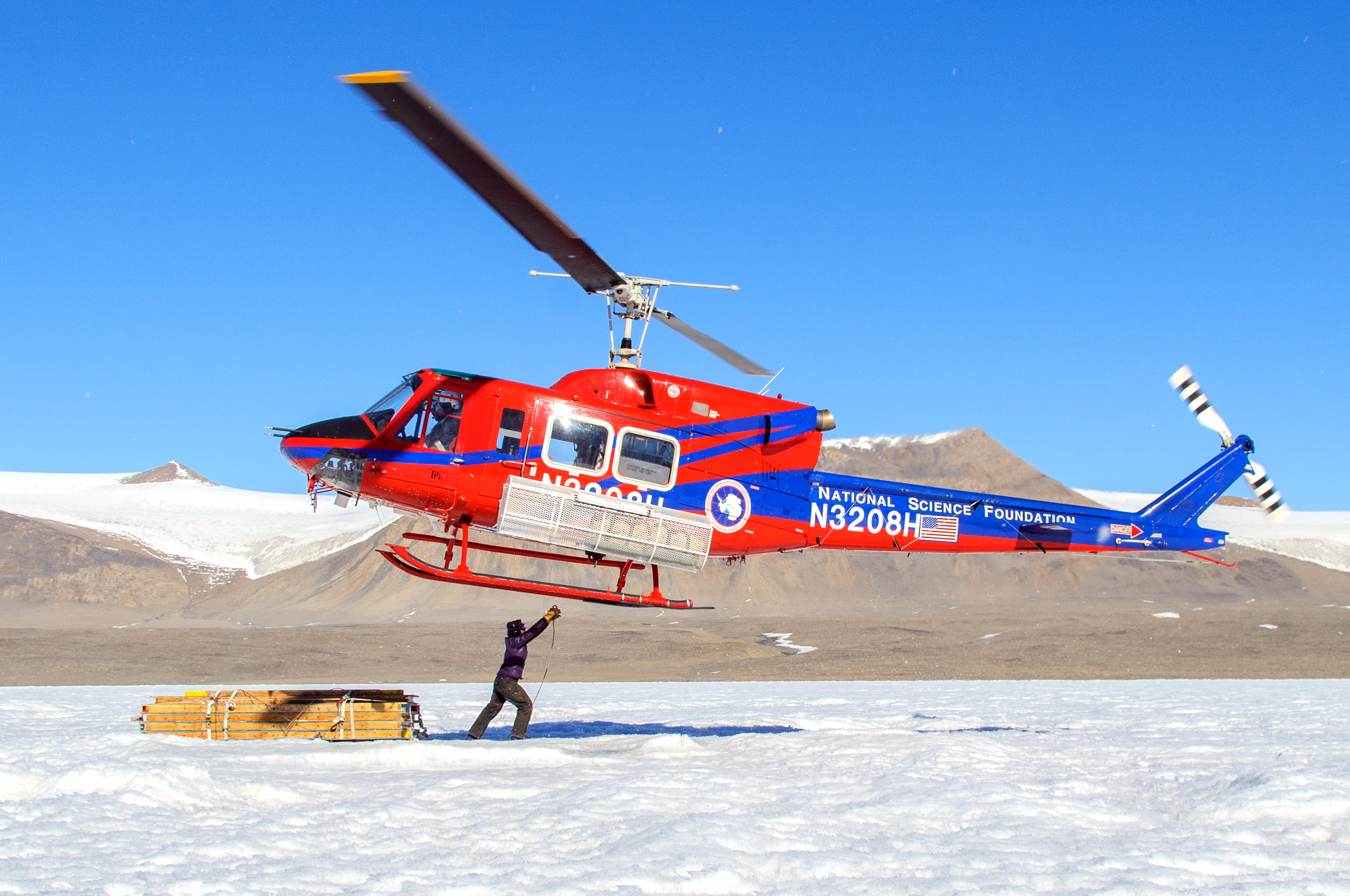 A person attaches a cable underneath a helicopter.