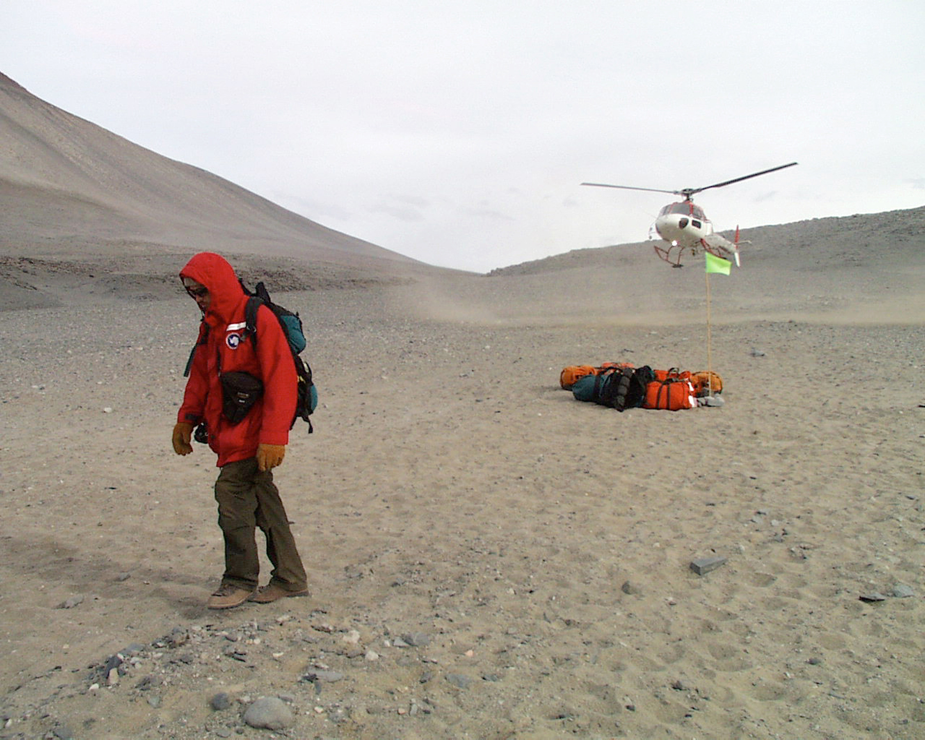 A helicopter lifts off while a person in a red coat walks away.