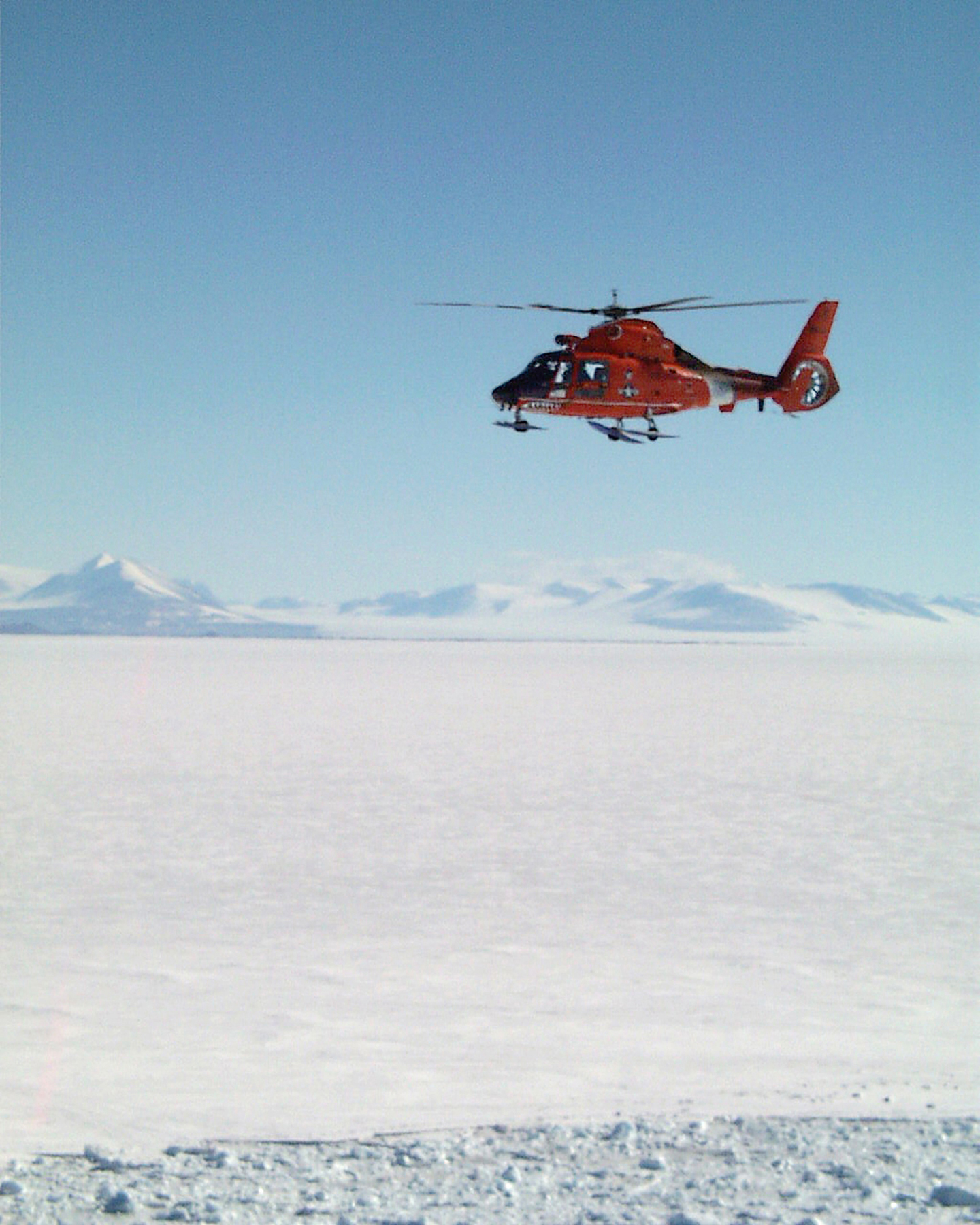 A helicopter flies over snow-covered terrain.