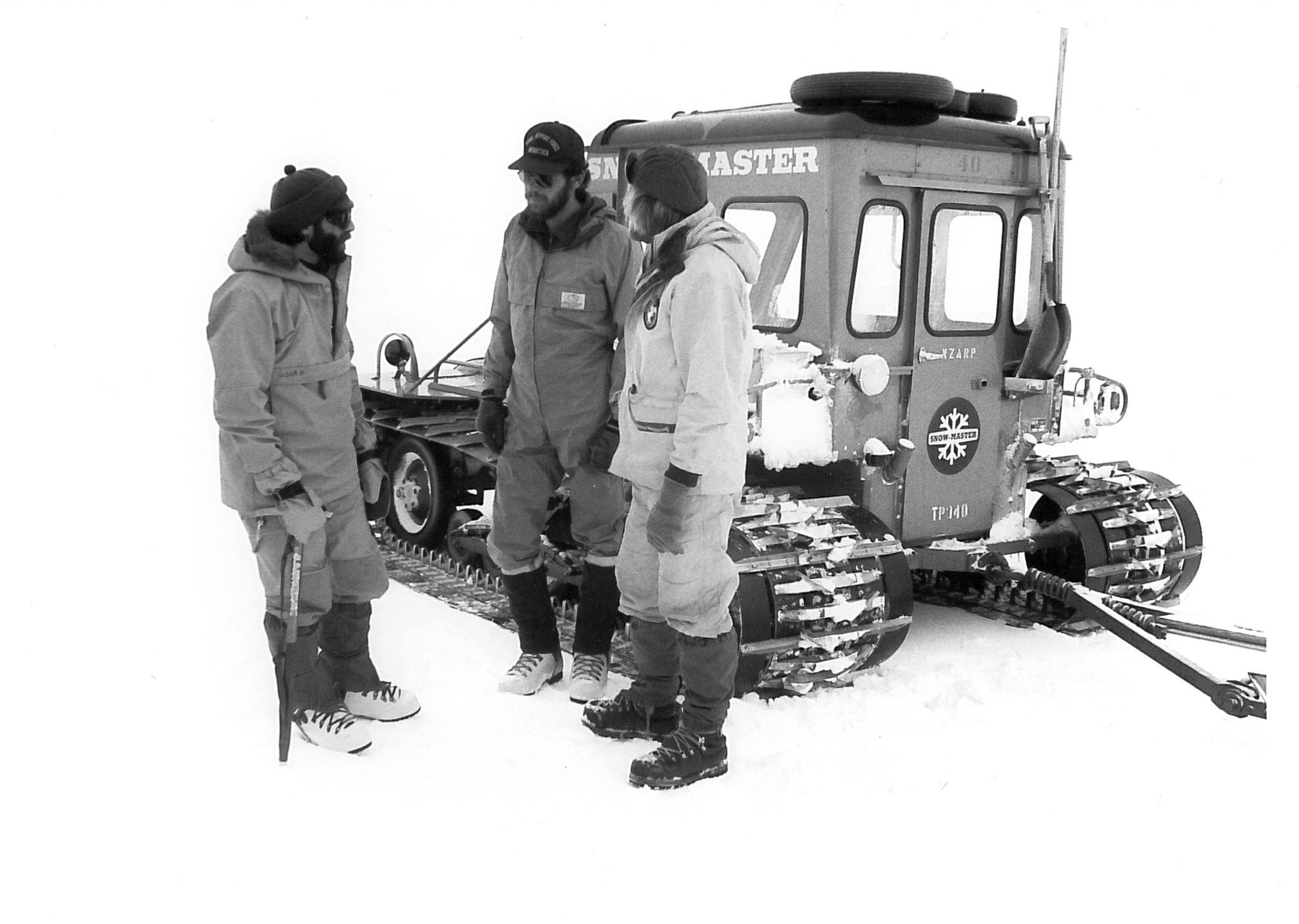 Three men standing in the snow next to a tractor.