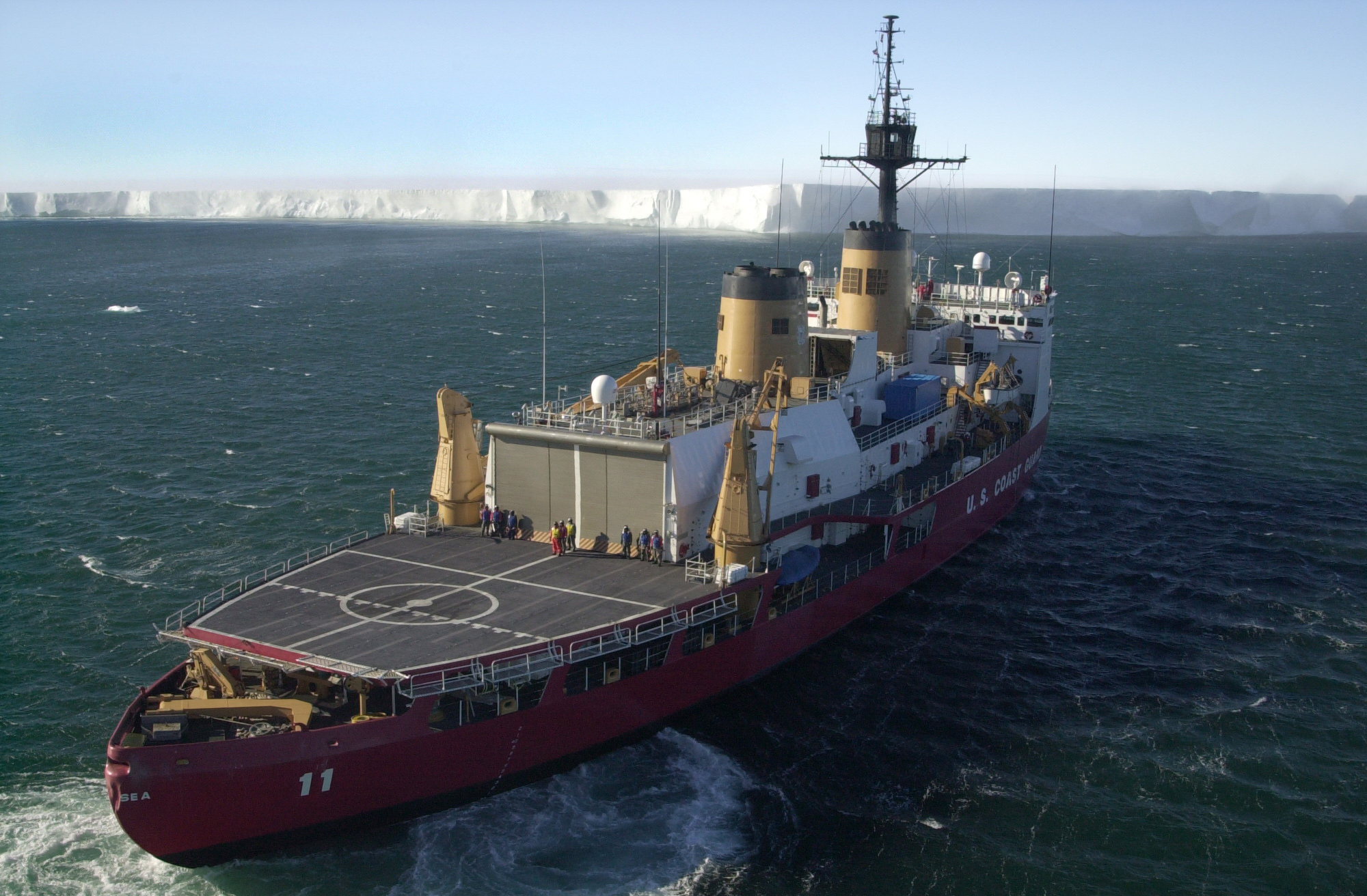 Aerial view of a ship approaching the edge of an enormous iceberg.