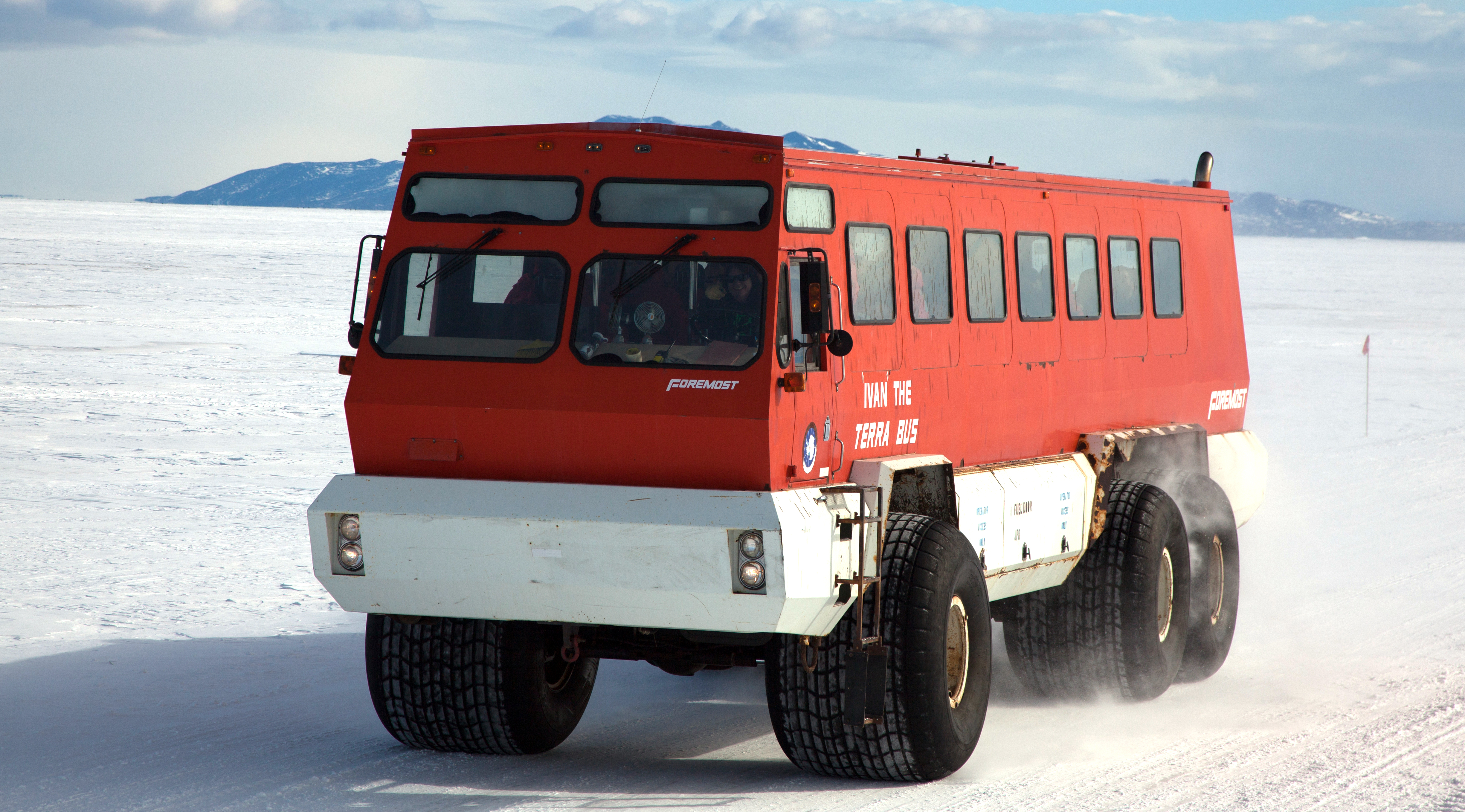 Red bus drives along snow road.