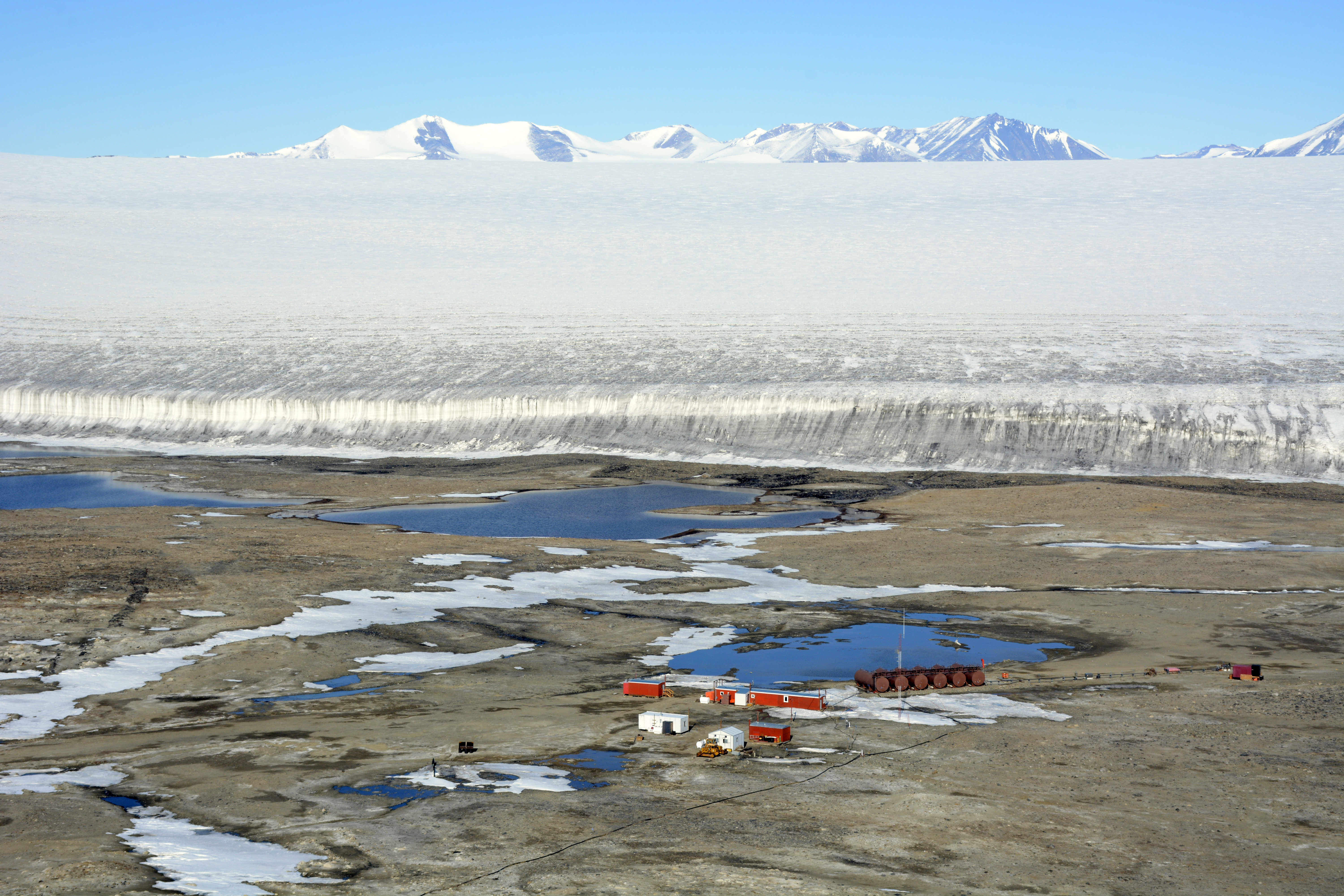 Aerial view of a camp with large ice sheet in the background.