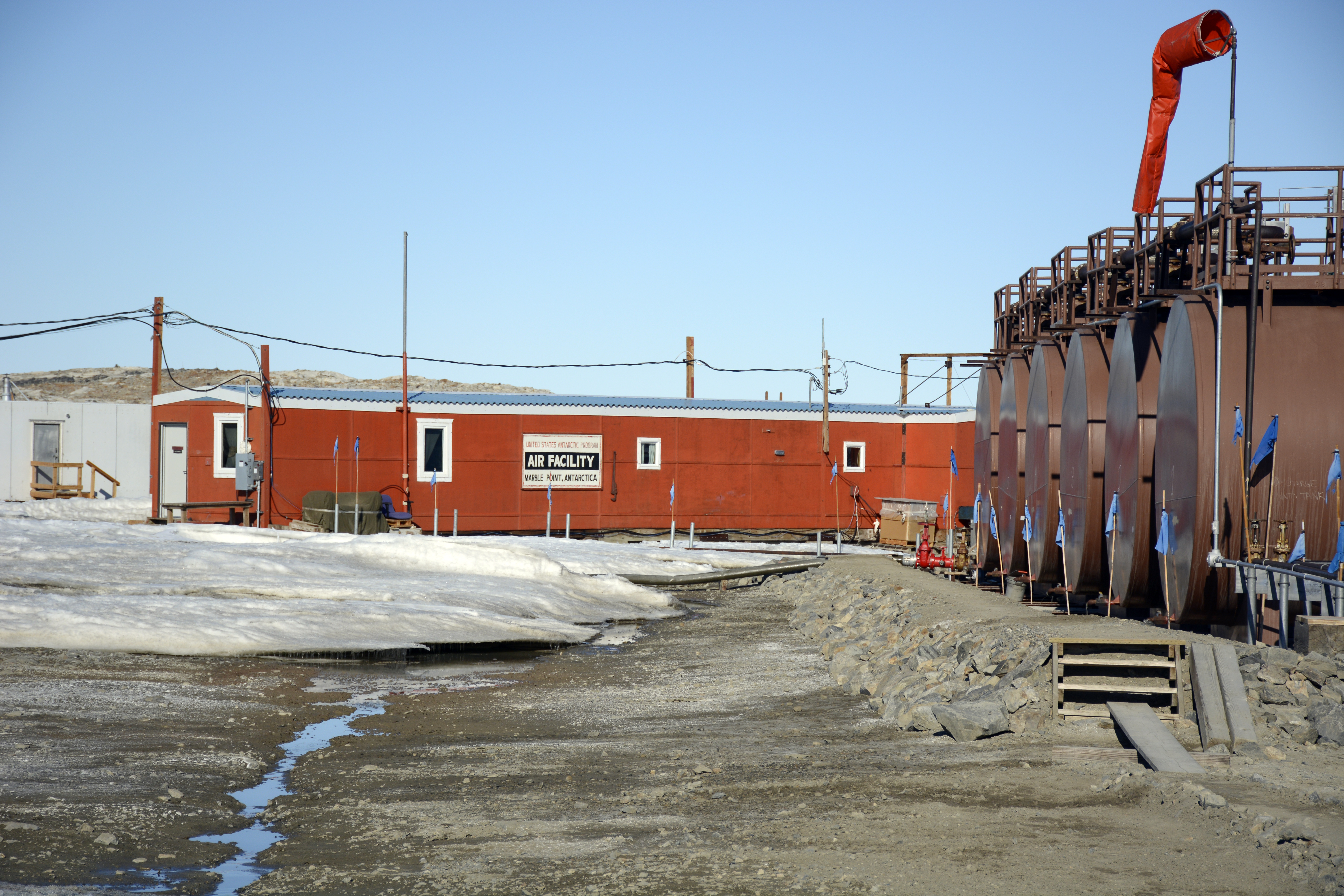 Row of fuel tanks sits in front of long orange building. 