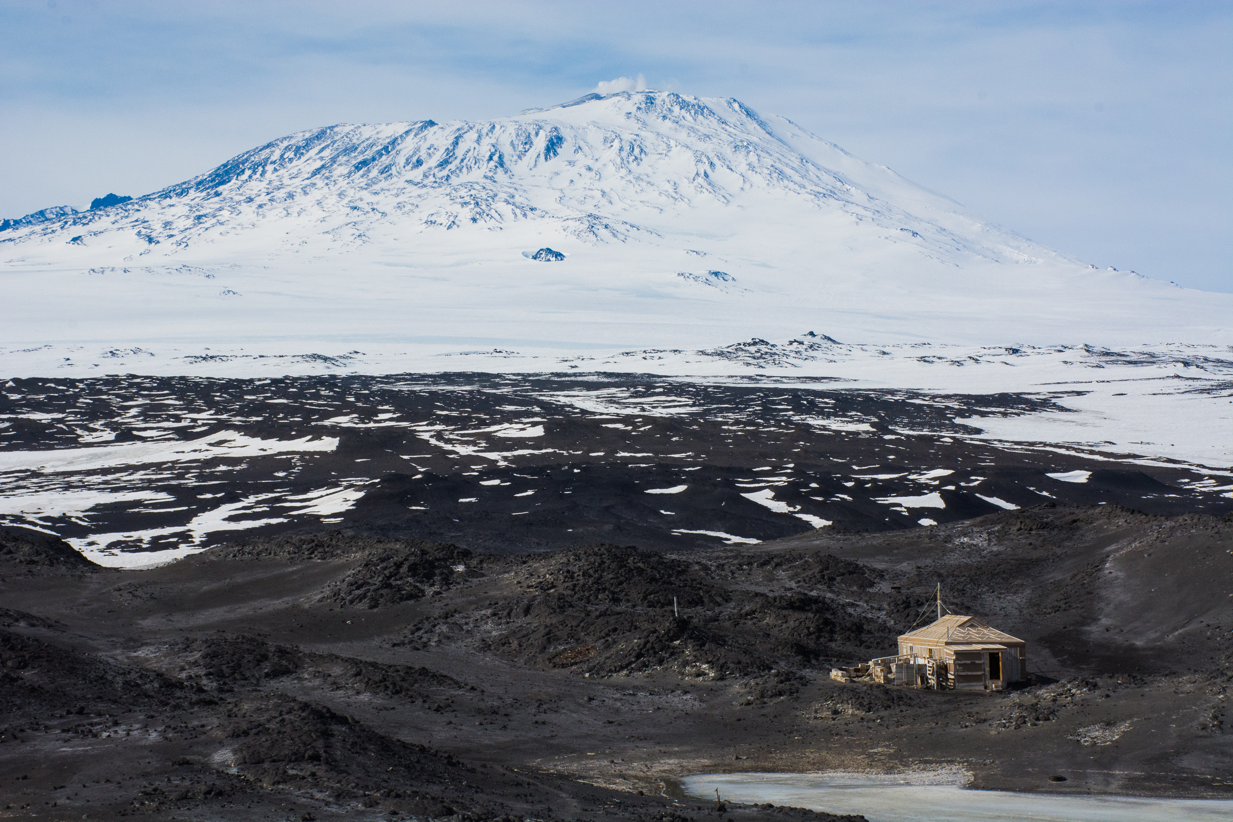 A small hut in front of a large snowy mountain