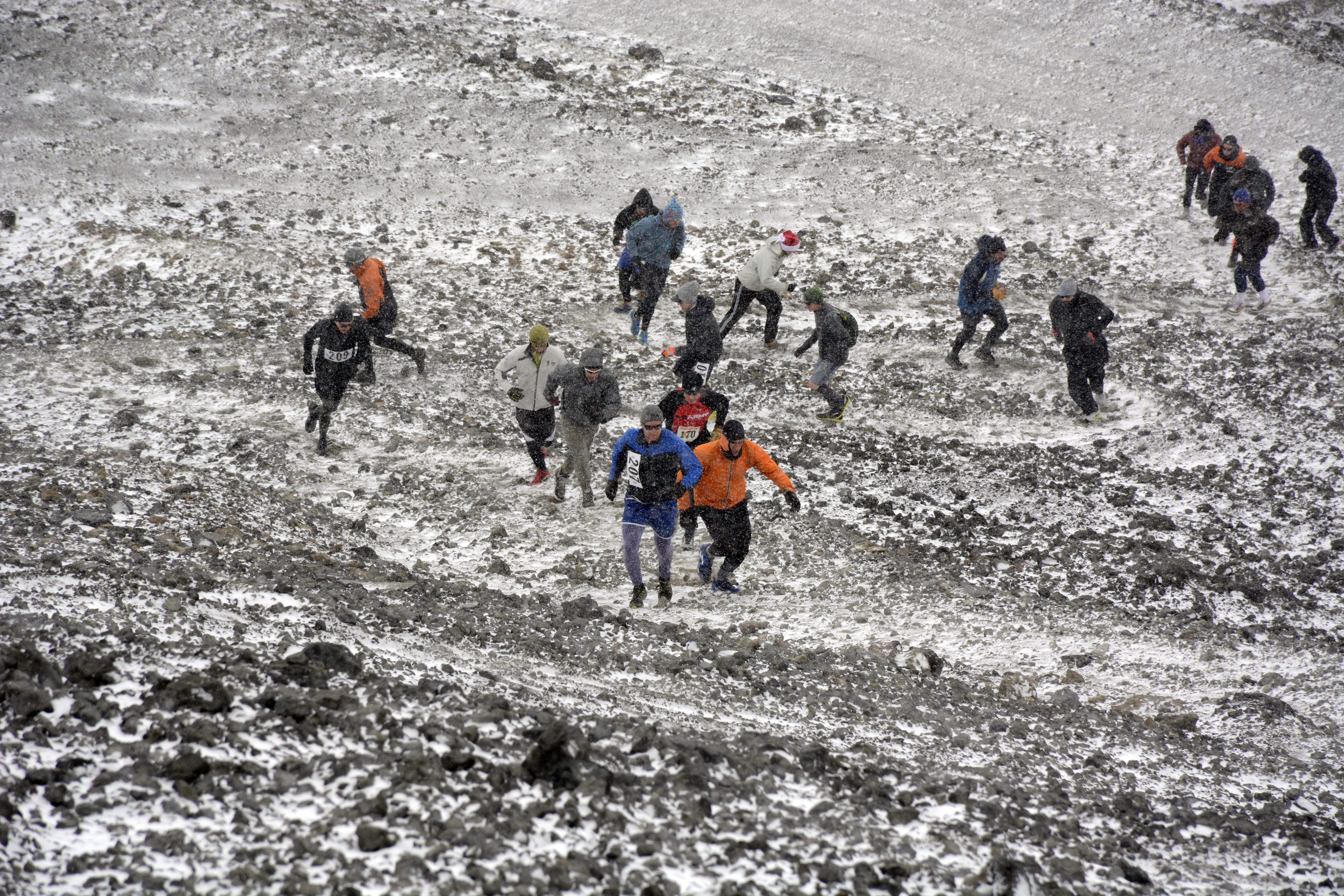 Line of people run up a hill in a snowstorm. 