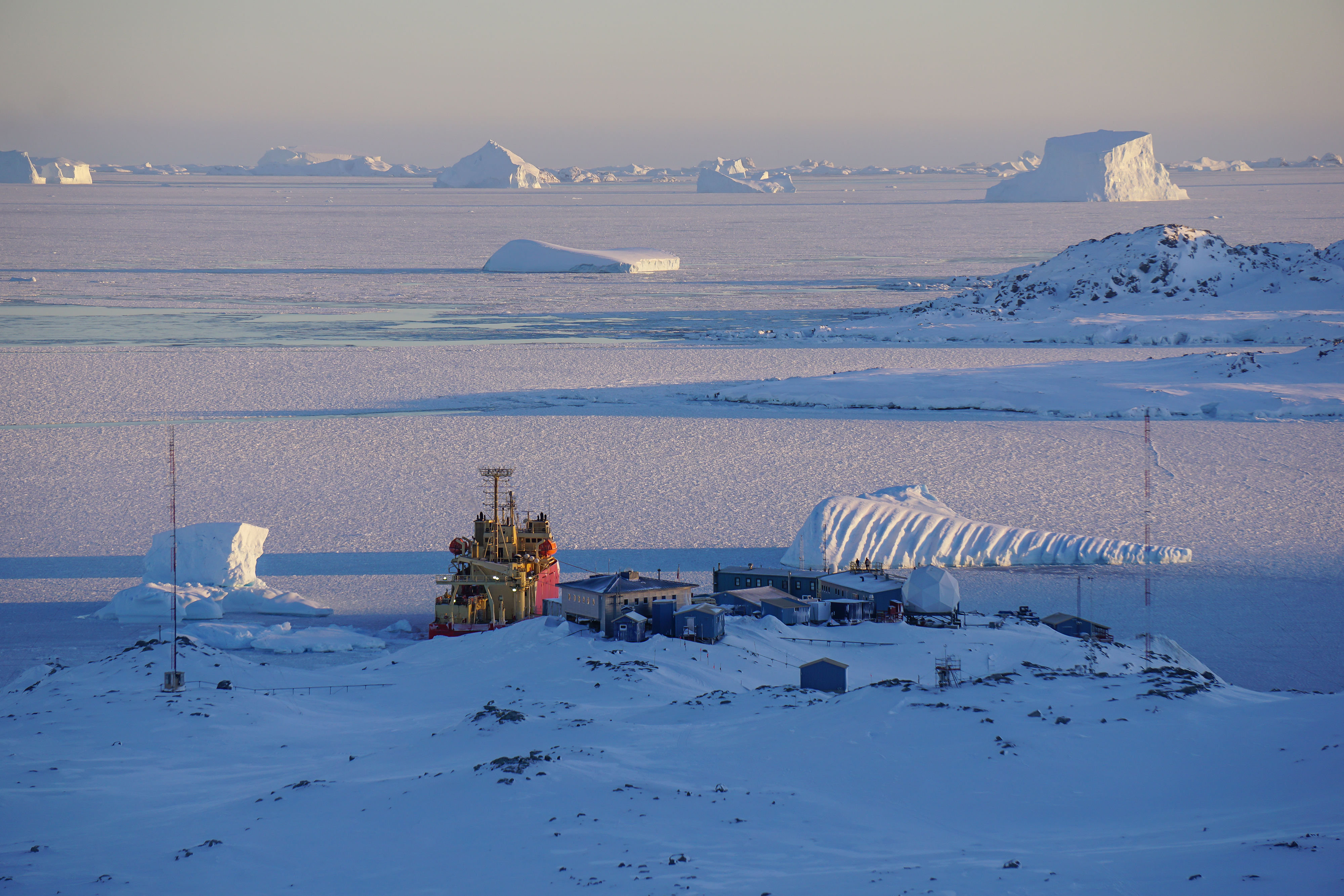 A snowy landscape with a ship and buildings.