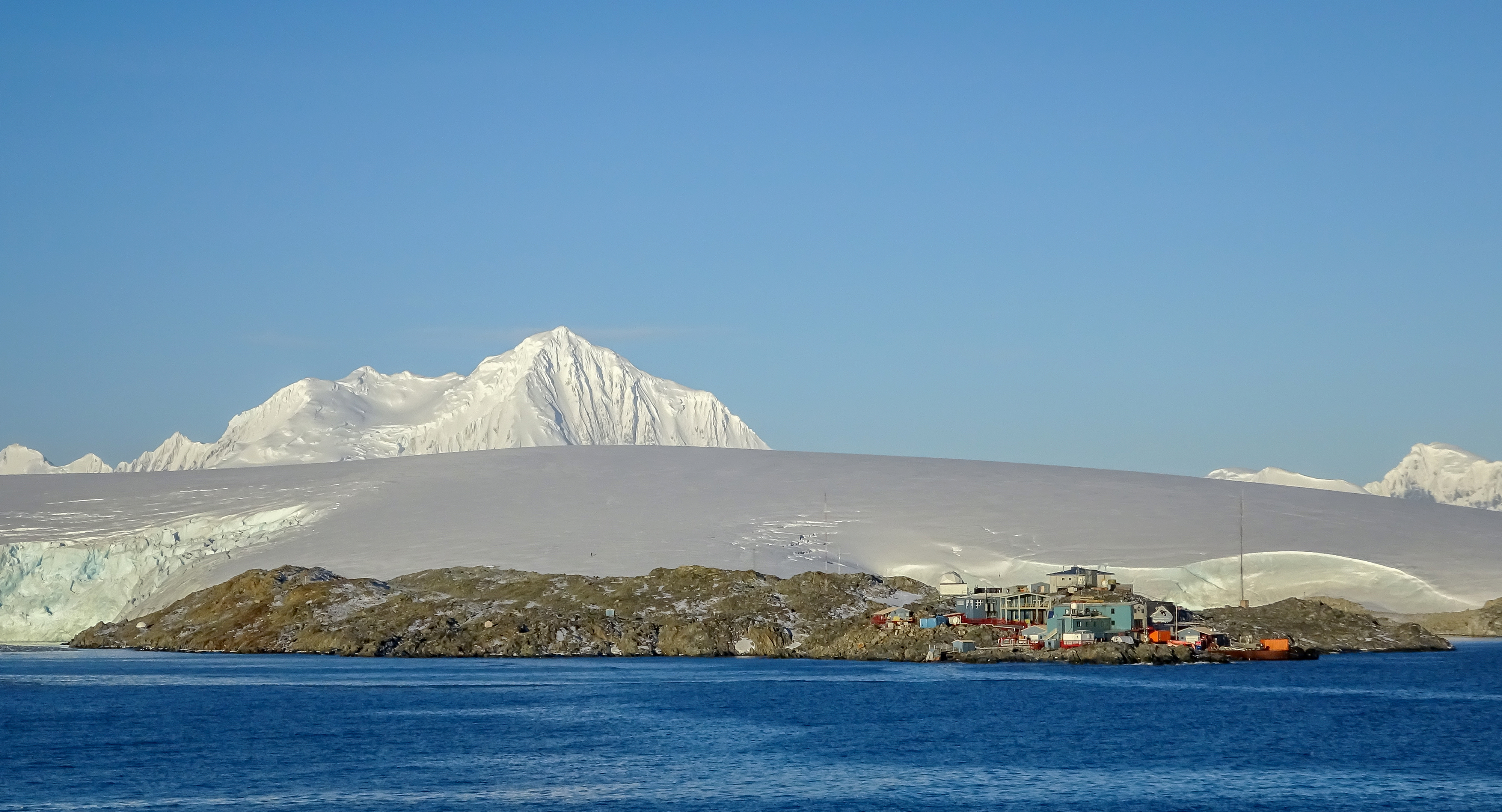 A view of a small station below a glacier and mountains.
