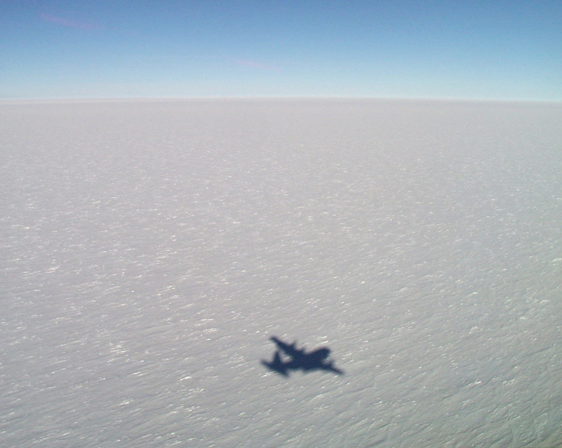 A shadow of an airplane on a vast expanse of snow.