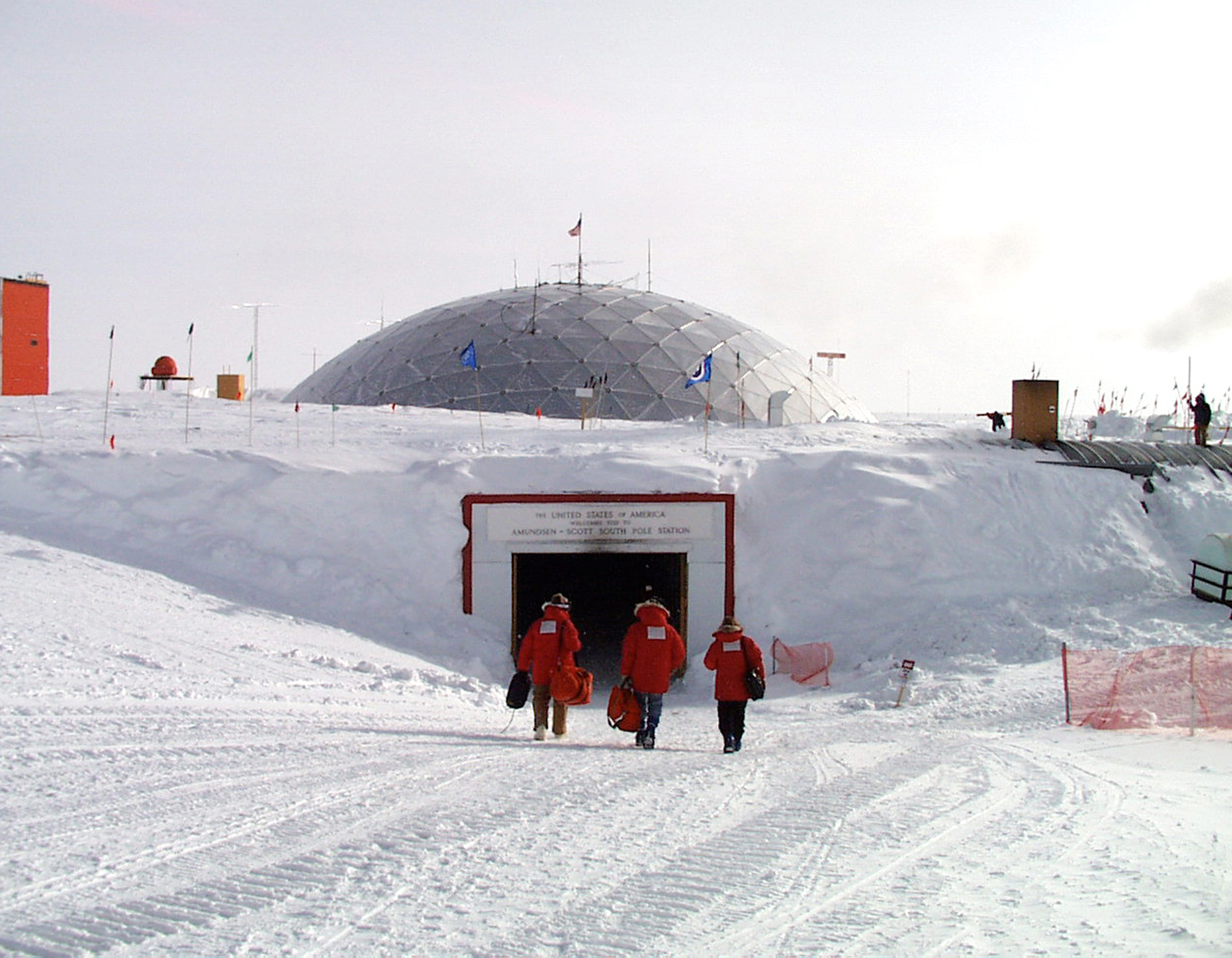 People walk into the entrance of a dome nearly buried in snow.