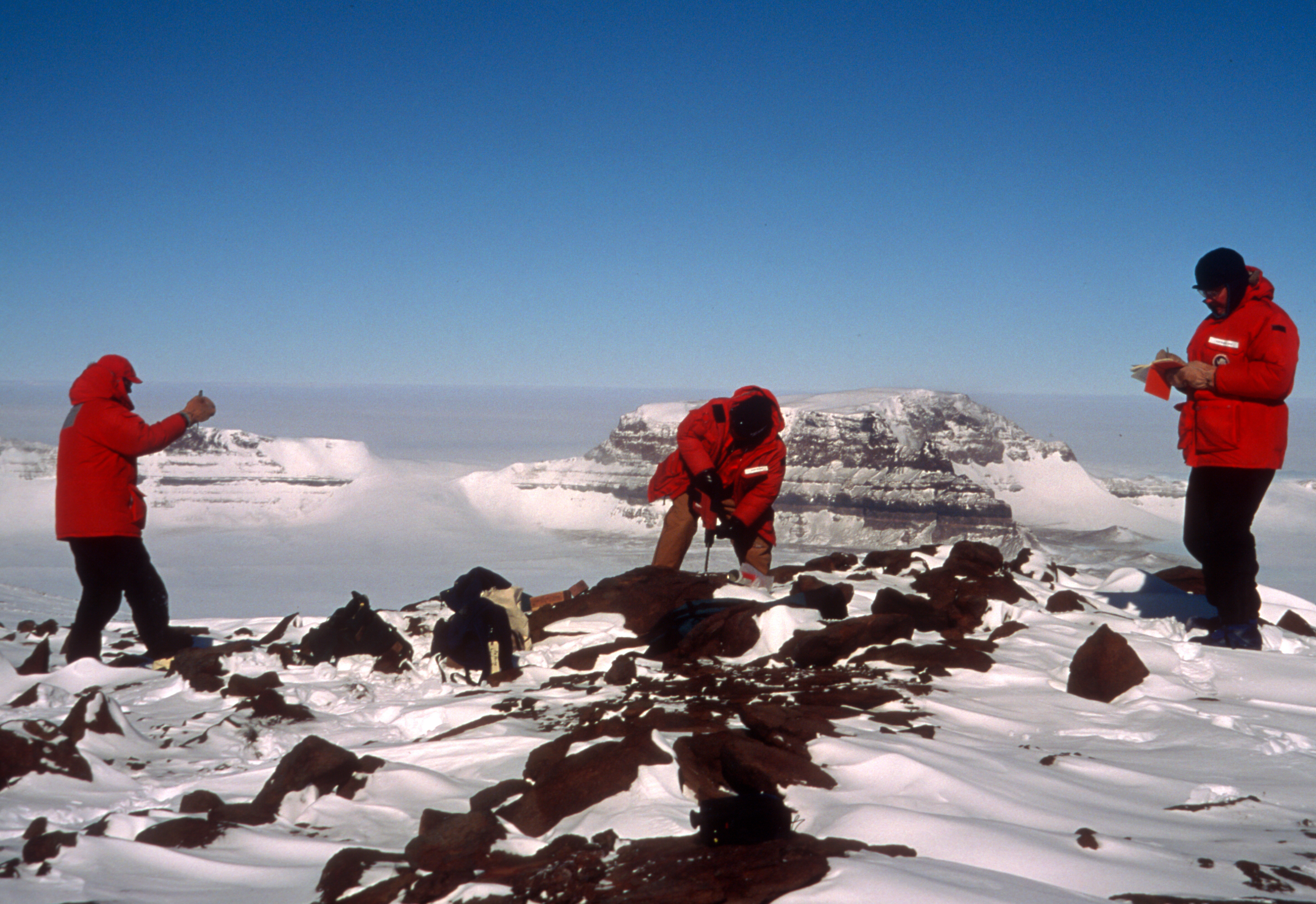 Three people on a rocky and snowy landscape.