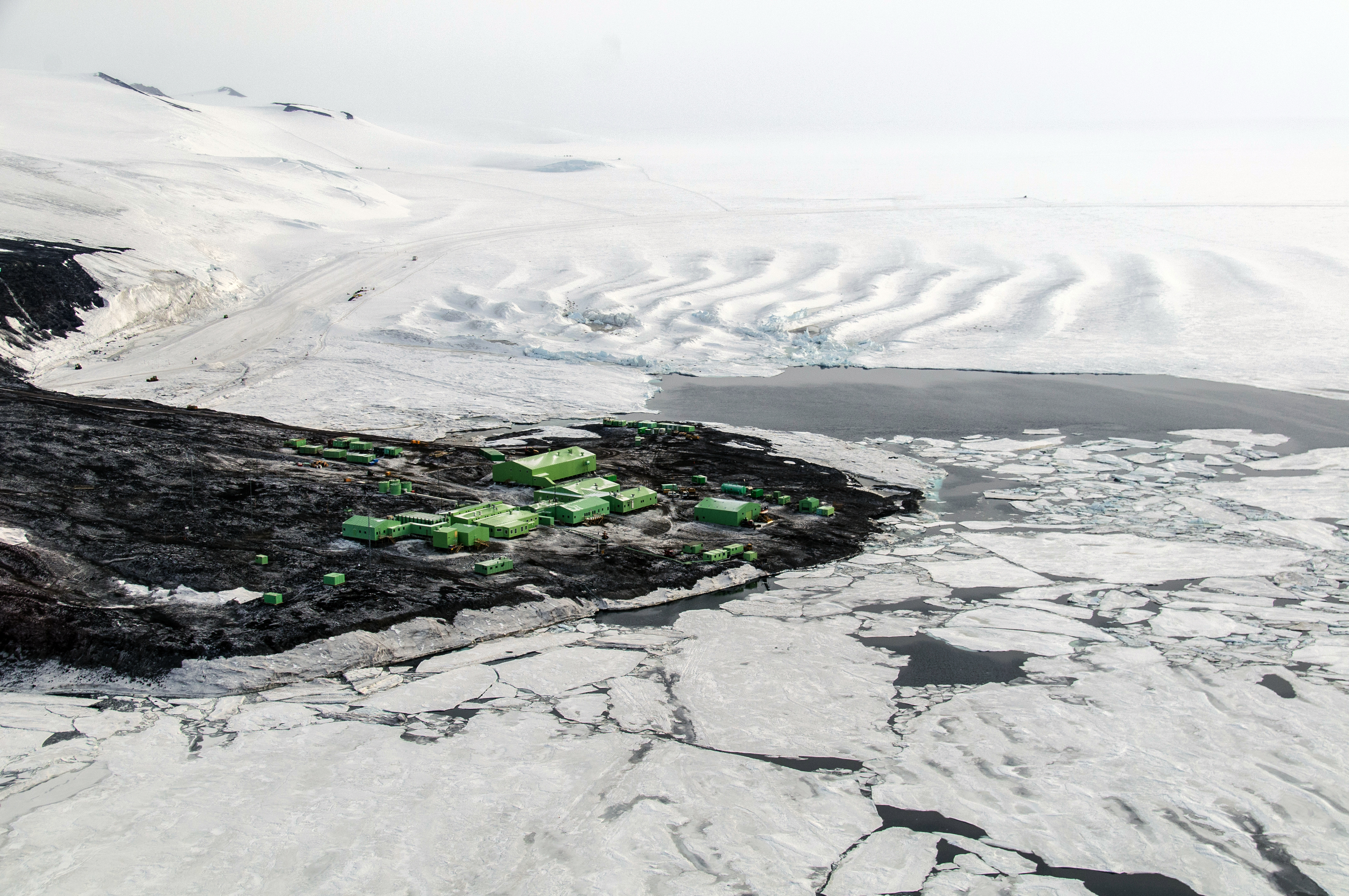 Small town of green buildings sits on a shore surrounded by ice.