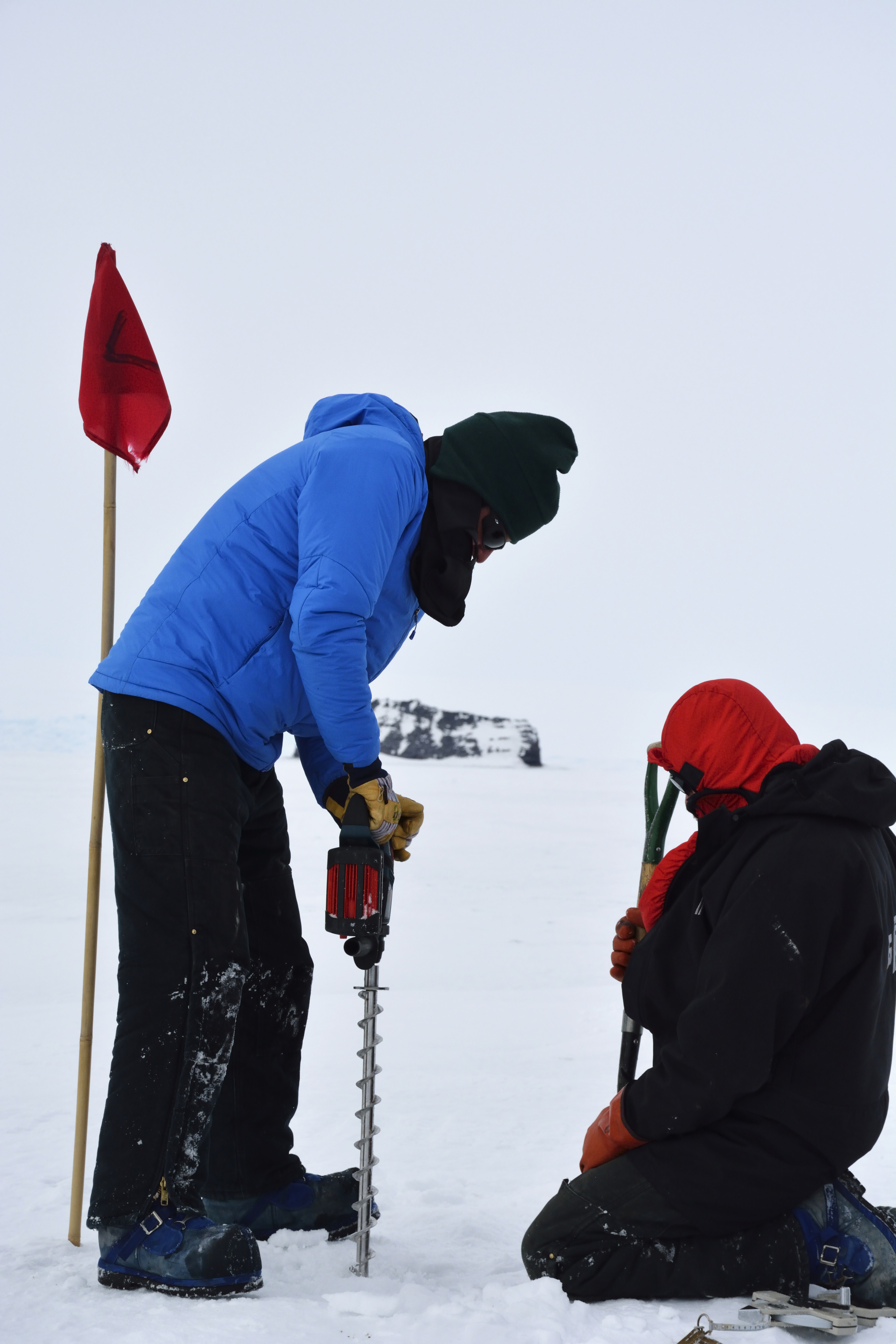 Person drills into ice while second person holds a shovel.