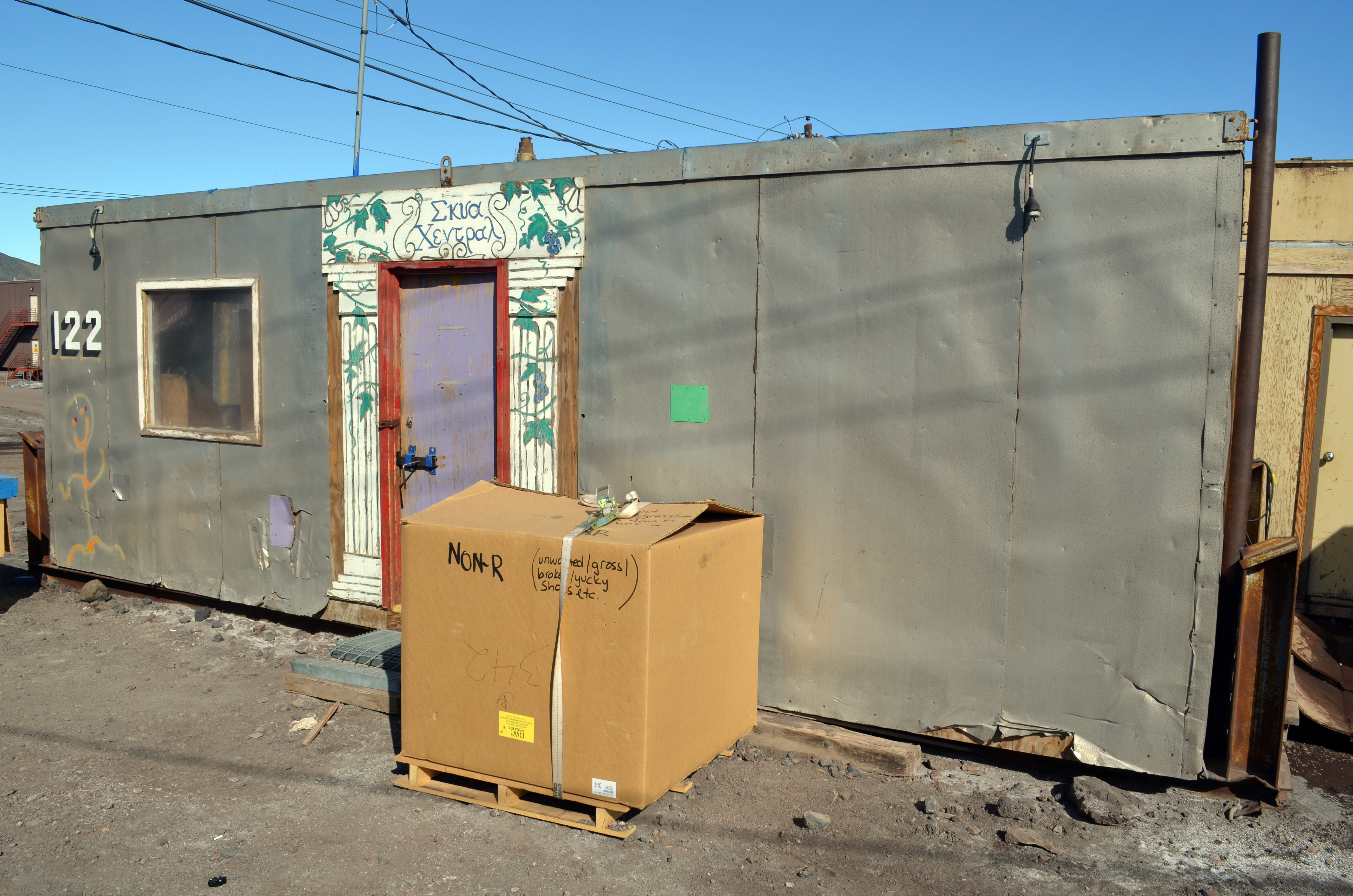 Large cardboard box sits in front of small building. 