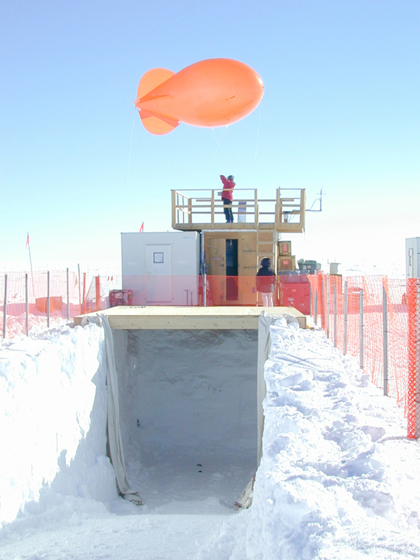 A small orange dirigible hovers above a snow-encased building.