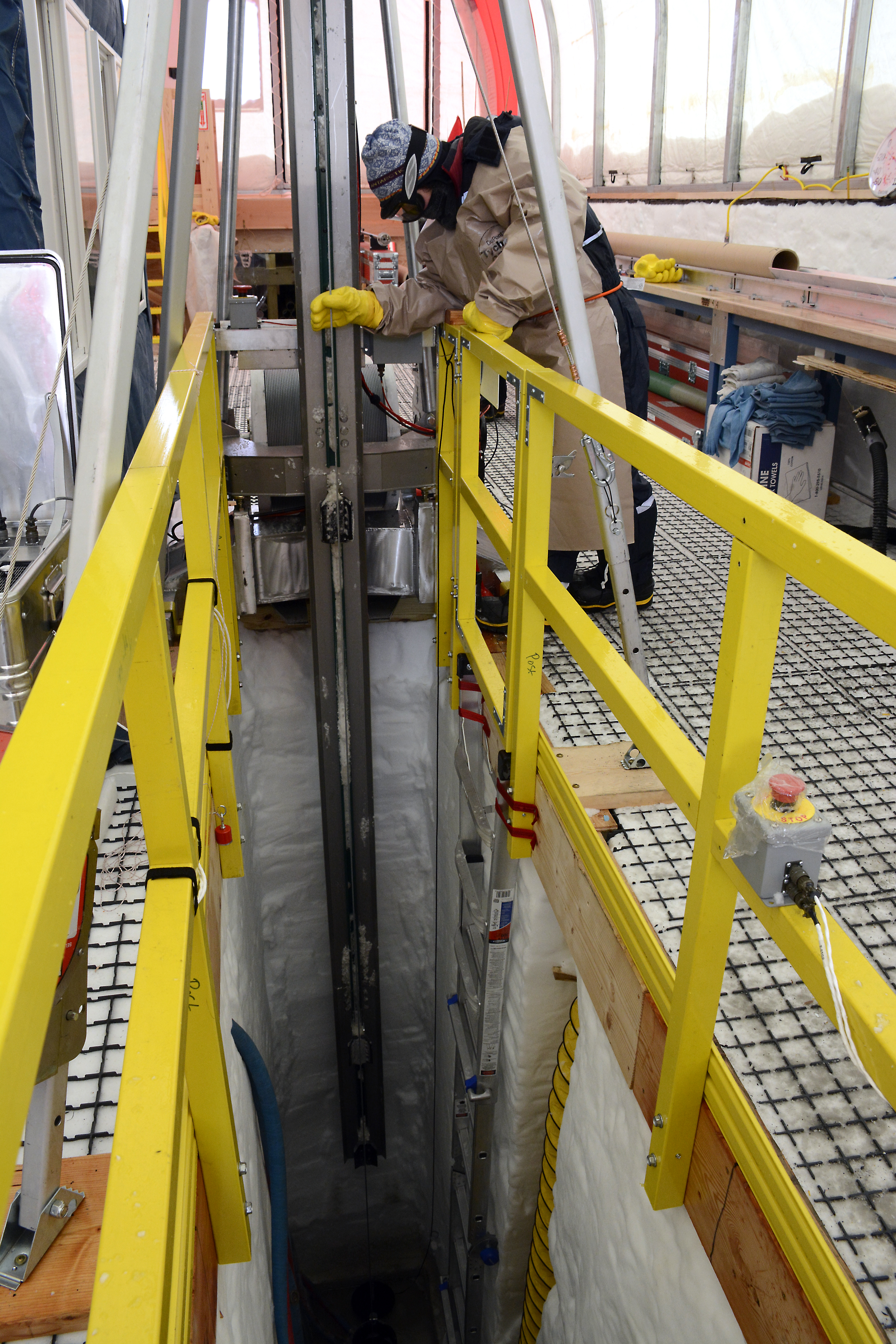 A person guides an ice core drill casing up from the hole.