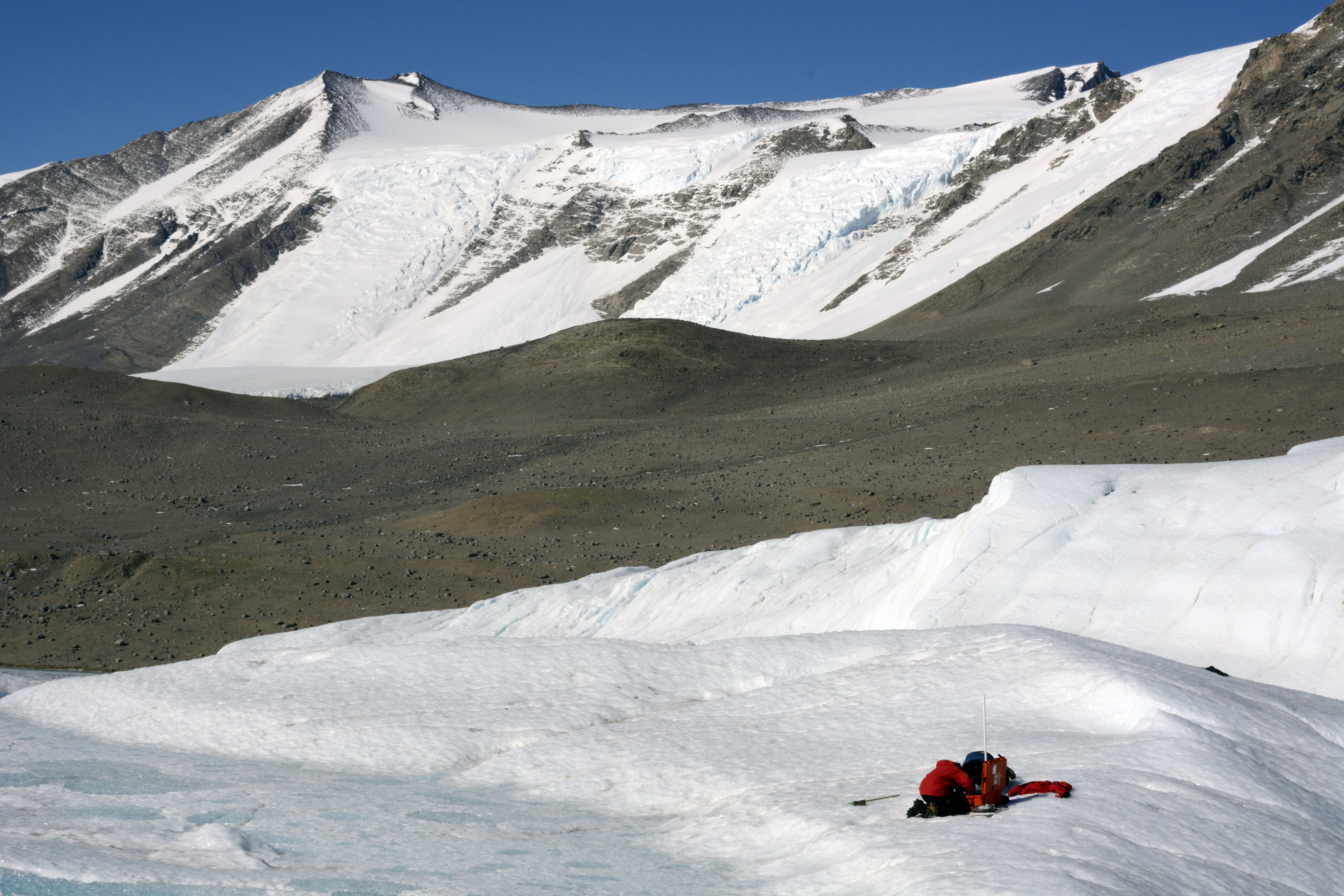 Two men work atop a glacier with electronics.