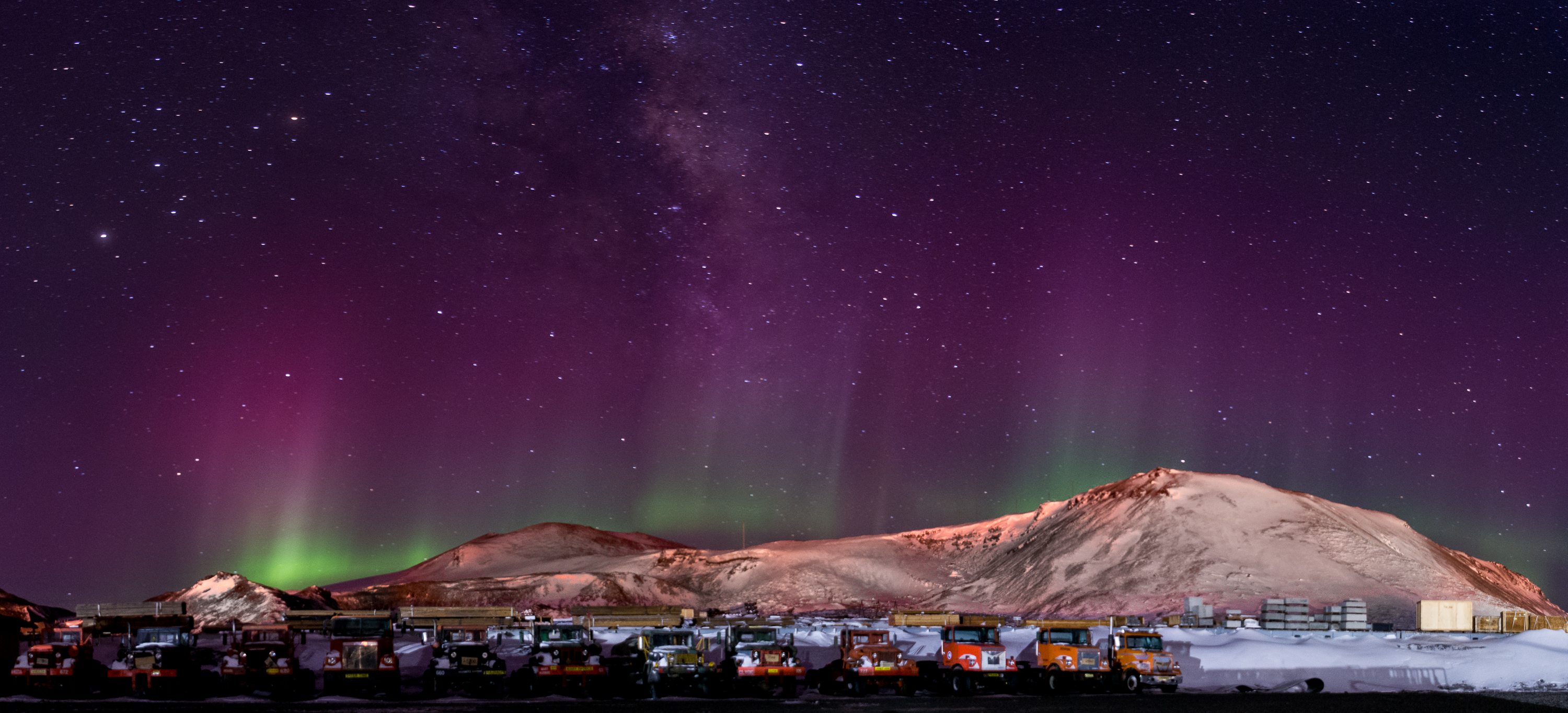 An aurora shimmers over a line of trucks at night.