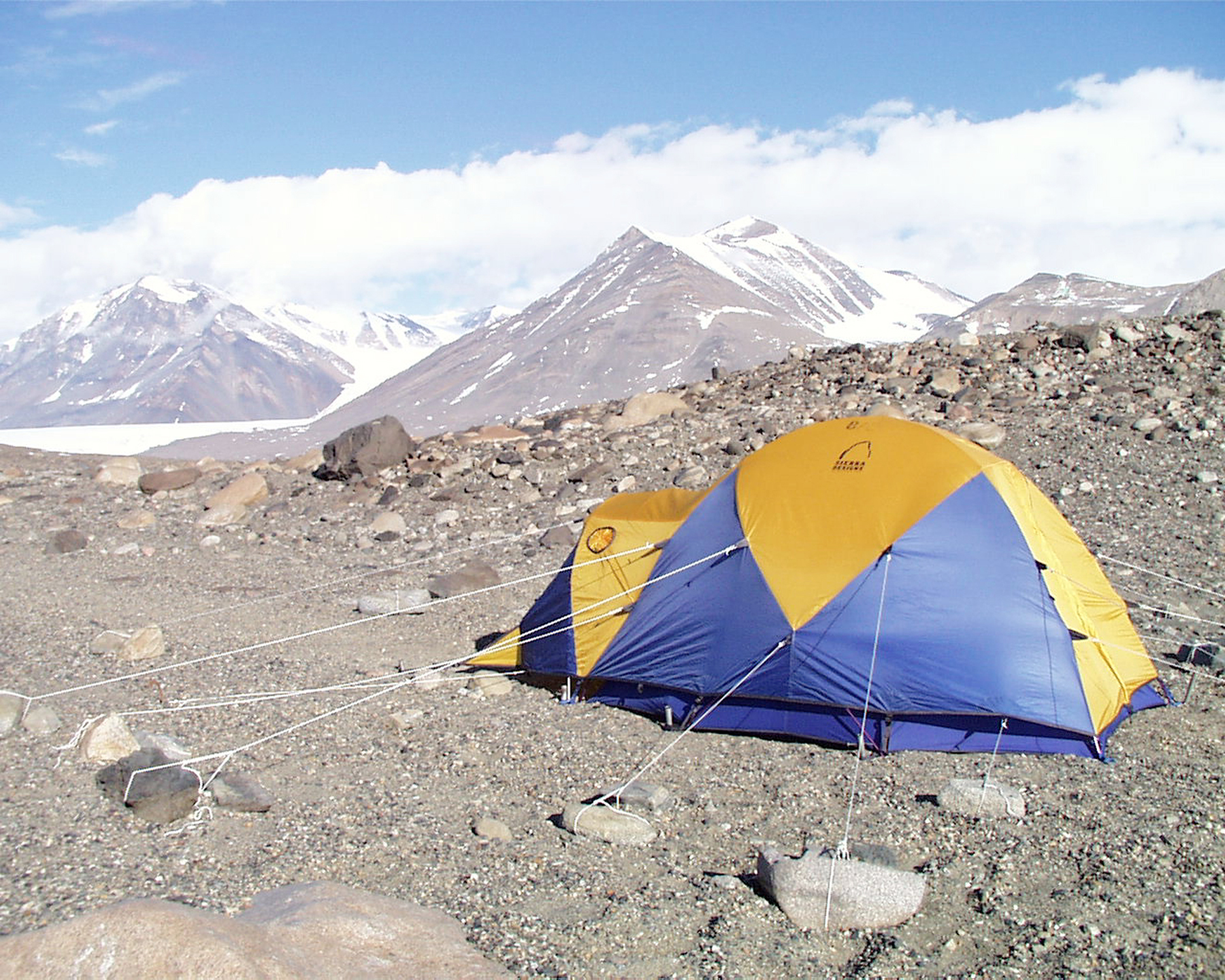 A blue and yellow tent sits on rocky terrain.