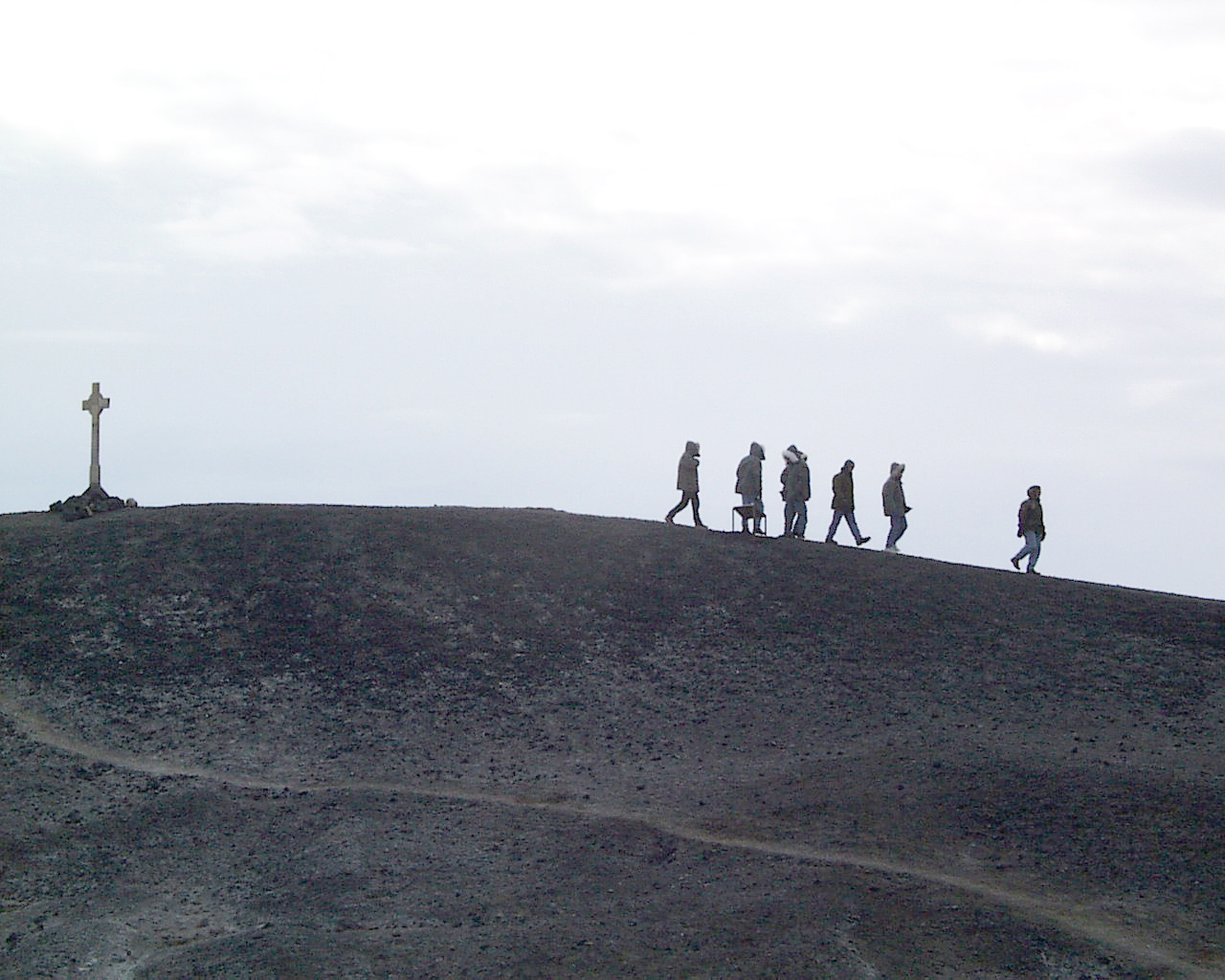 A distant view of people walking away from a cross on a hill.